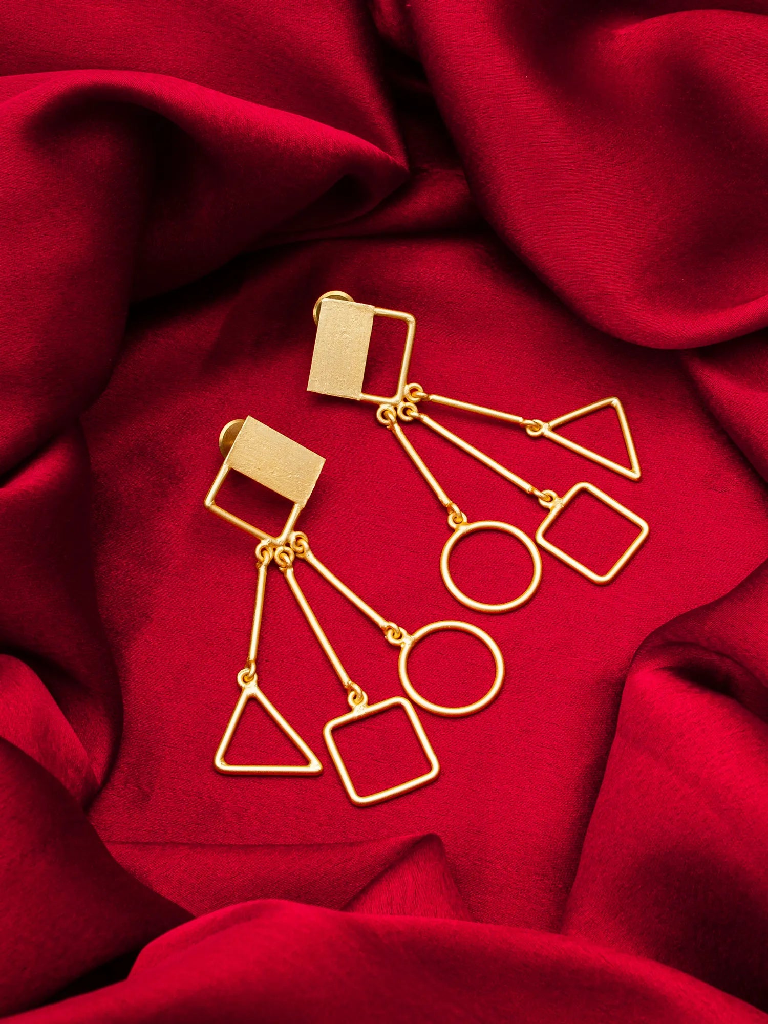 Gold geometric earrings on a red fabric background