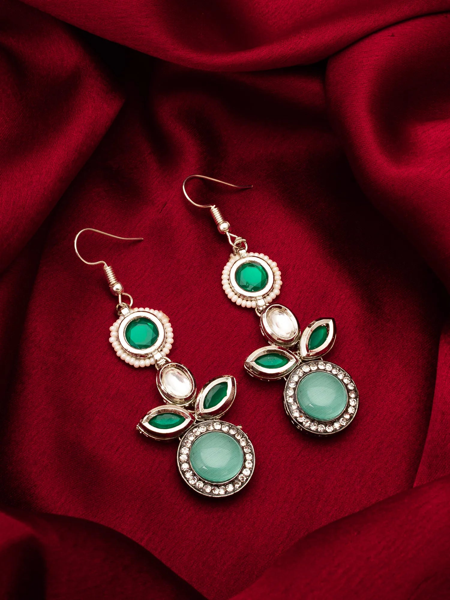 Pair of earrings with green and turquoise stones on a red fabric background