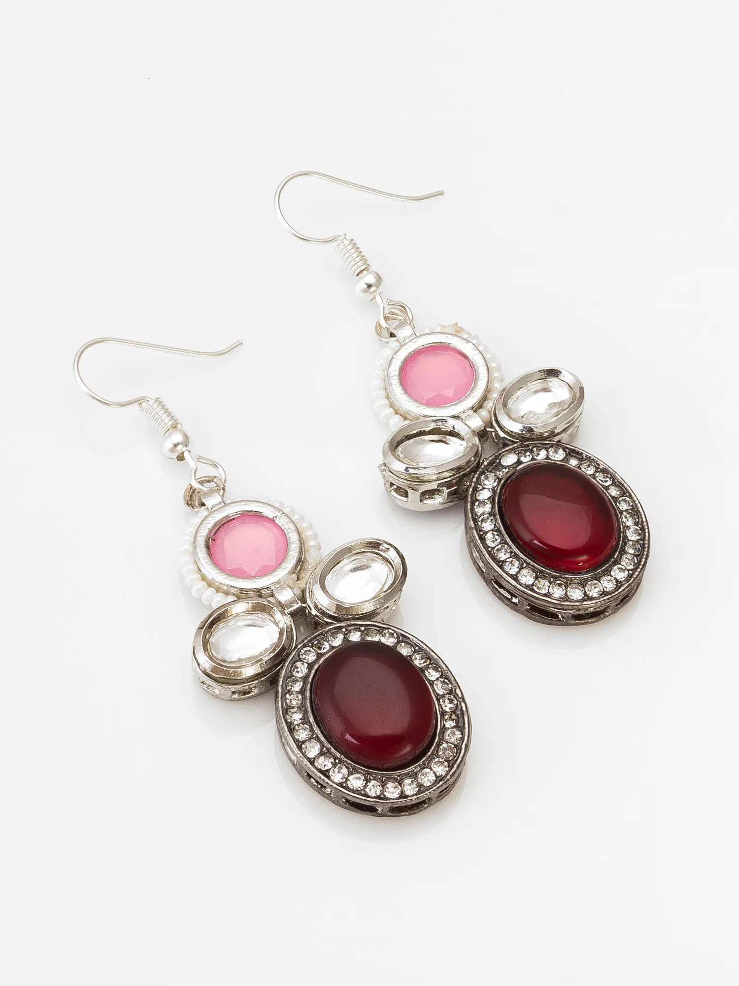 A pair of silver-toned dangle earrings featuring oval pink and deep red cabochon stones surrounded by small clear rhinestones, shown on a plain white background.