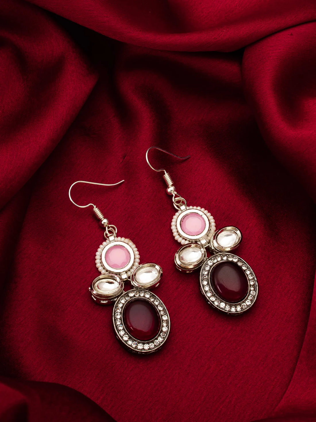 Pair of earrings with pink and red stones on a red fabric background