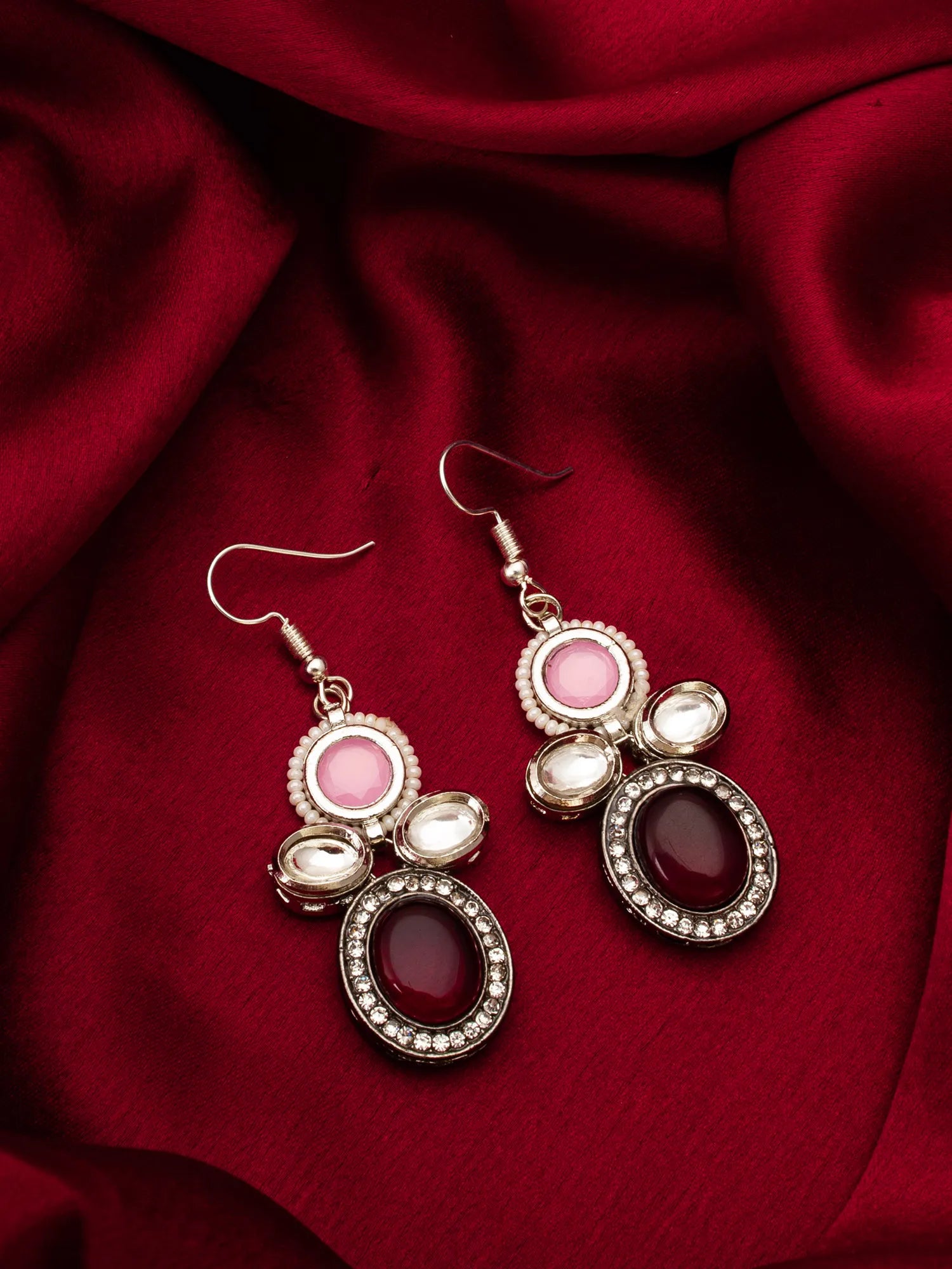 Pair of earrings with pink and red stones on a red fabric background