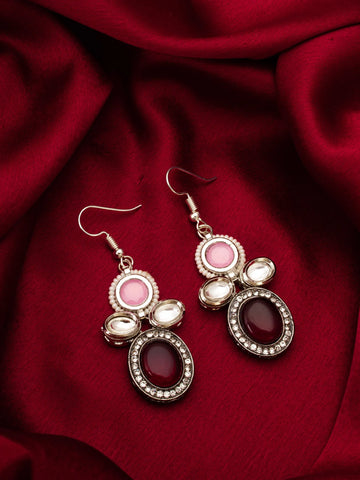 Pair of earrings with pink and red stones on a red fabric background