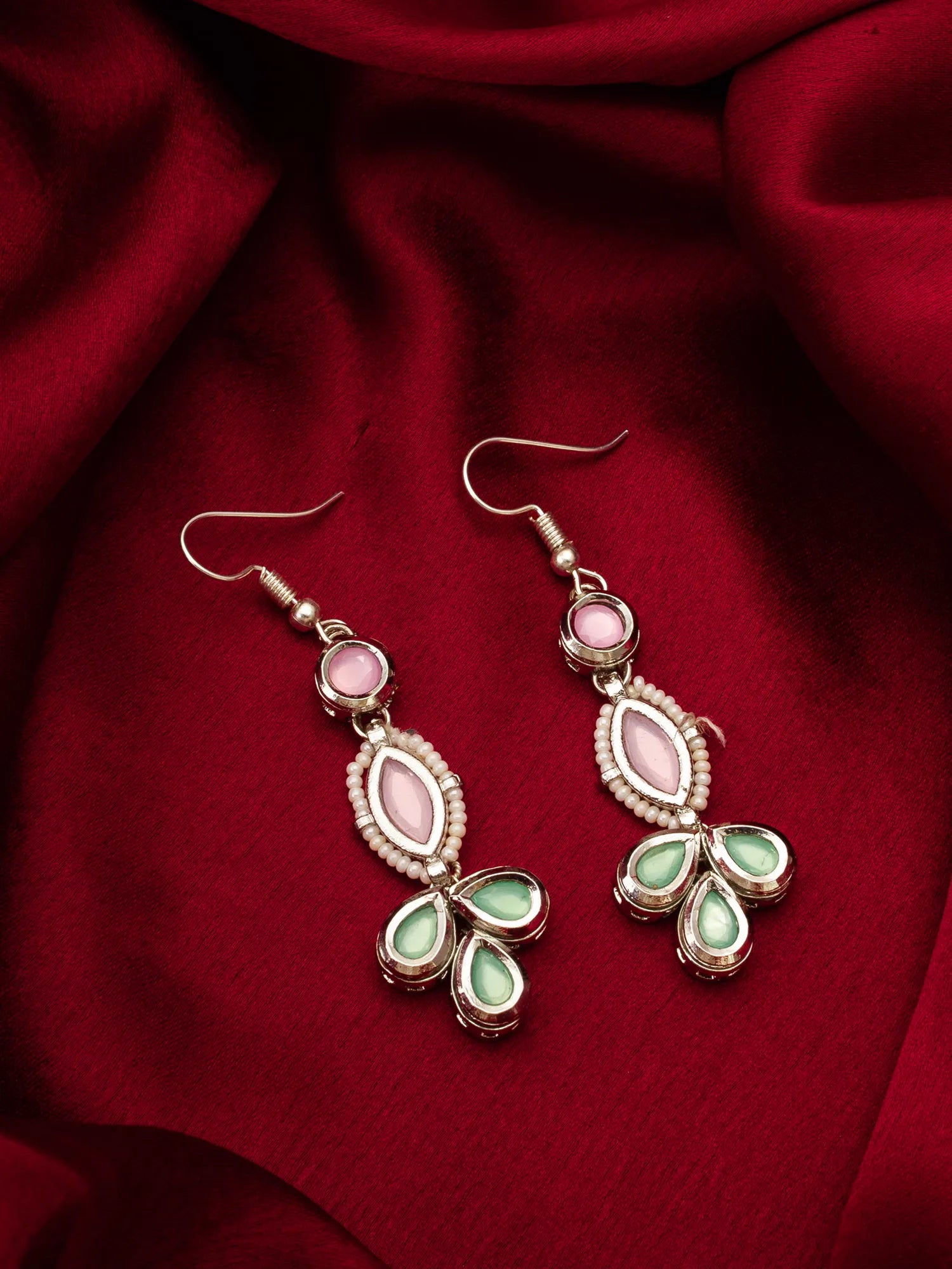 Pair of earrings with pink and green stones on a red fabric background