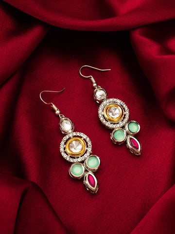 A pair of gold and silver dangle earrings with green and pink stones, displayed on a draped deep red fabric background.