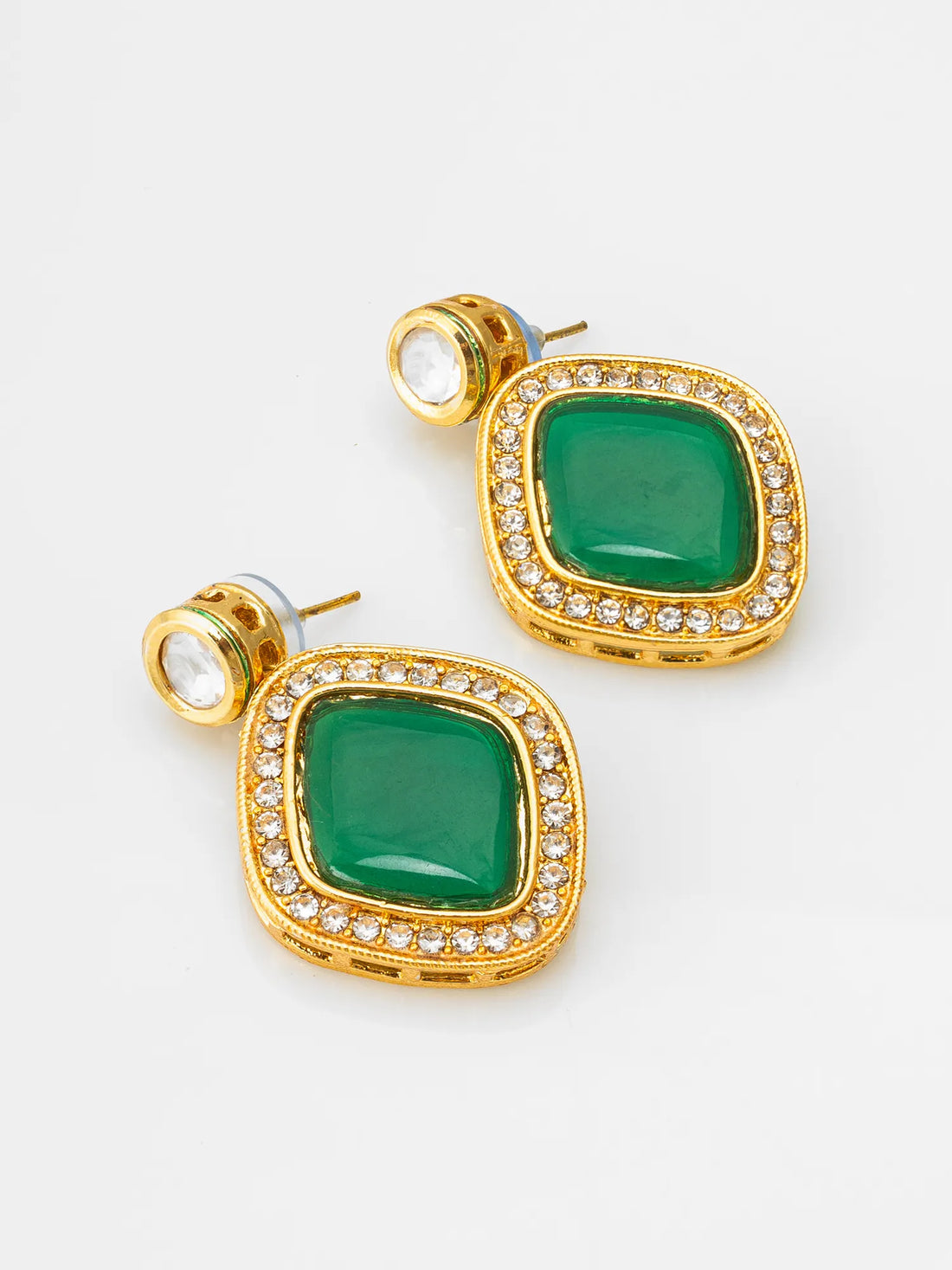 A pair of gold-plated statement earrings featuring large green marquise-shaped stones surrounded by small clear crystals, displayed on a dark green satin fabric background.