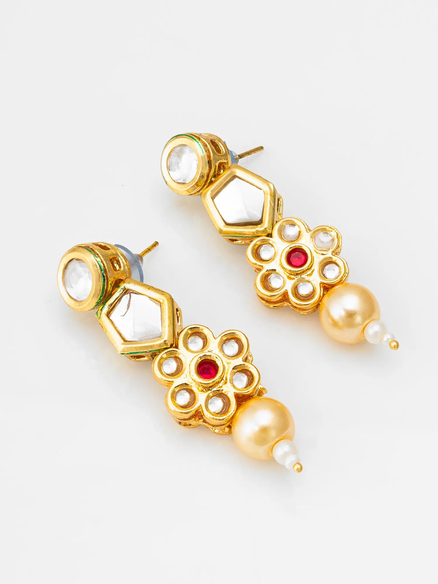 A pair of gold-plated kundan earrings featuring white stone clusters, a central red stone, and a dangling white pearl bead, shown on a light gray background.