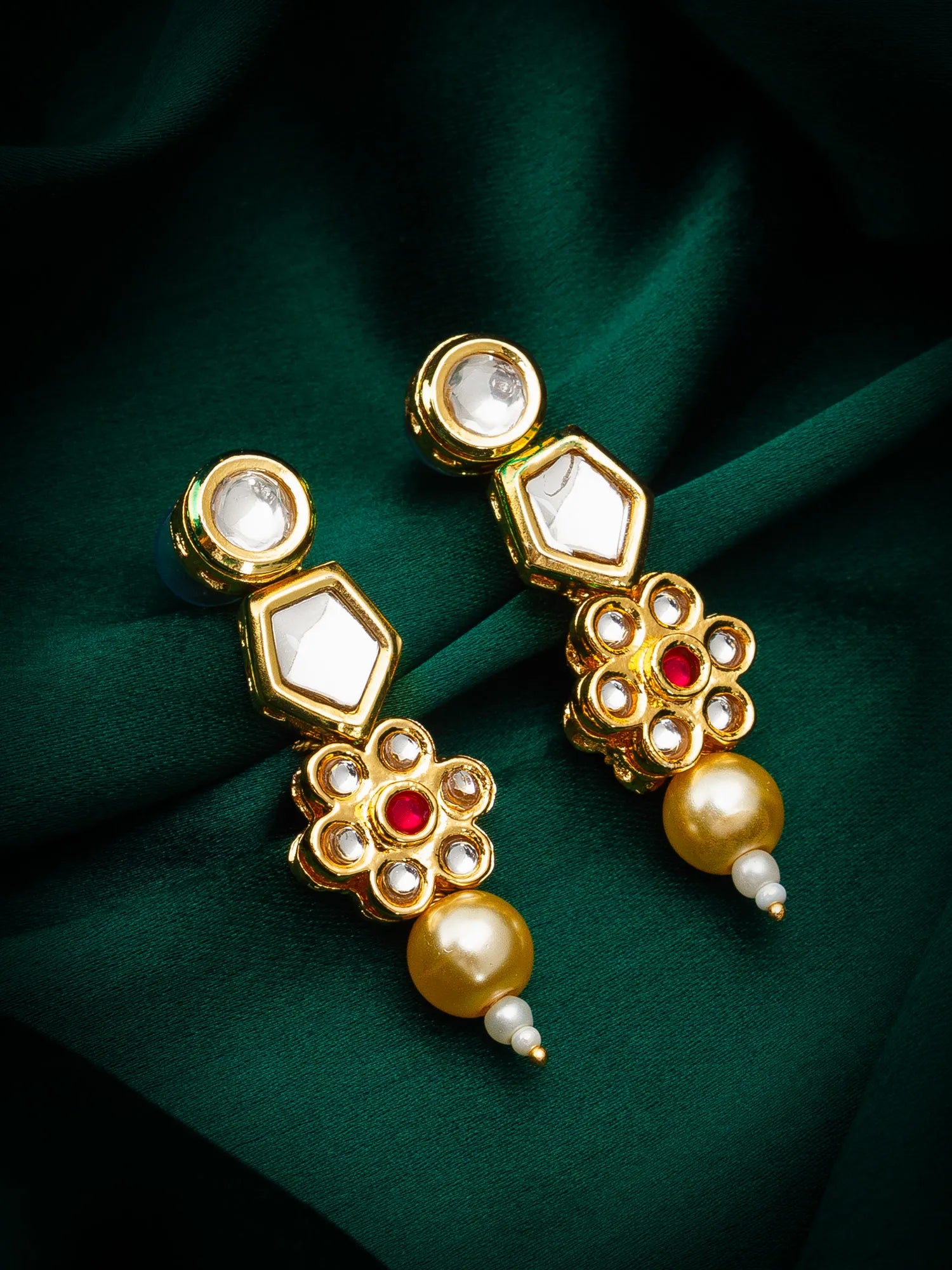 Gold earrings with pearls and red stones on a green fabric background