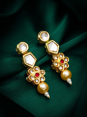 Gold earrings with pearls and red stones on a green fabric background