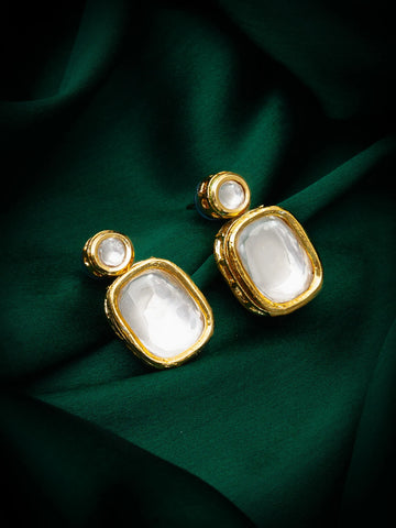 Gold and white earrings on a green fabric background