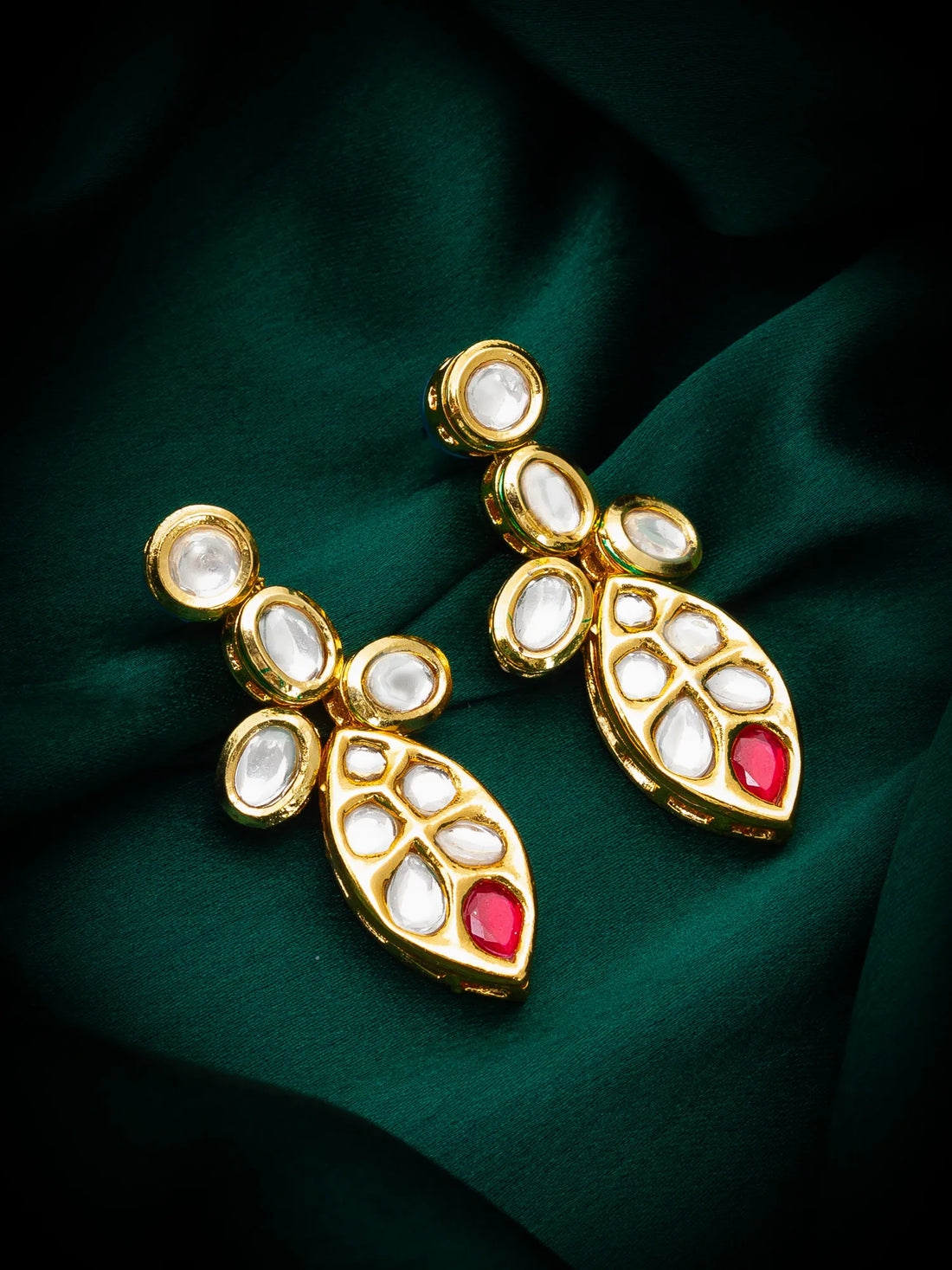 Gold earrings with red stones on a green fabric background