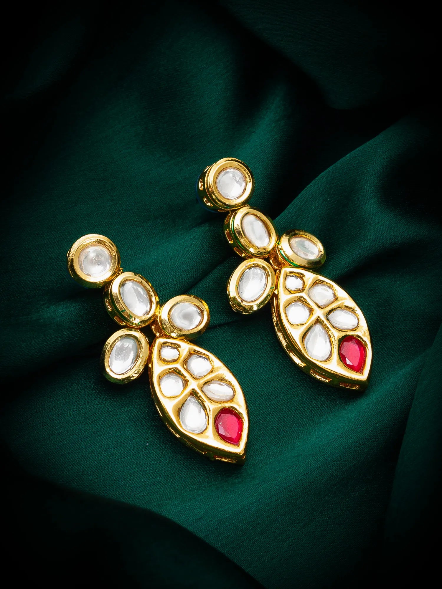Gold earrings with red stones on a green fabric background