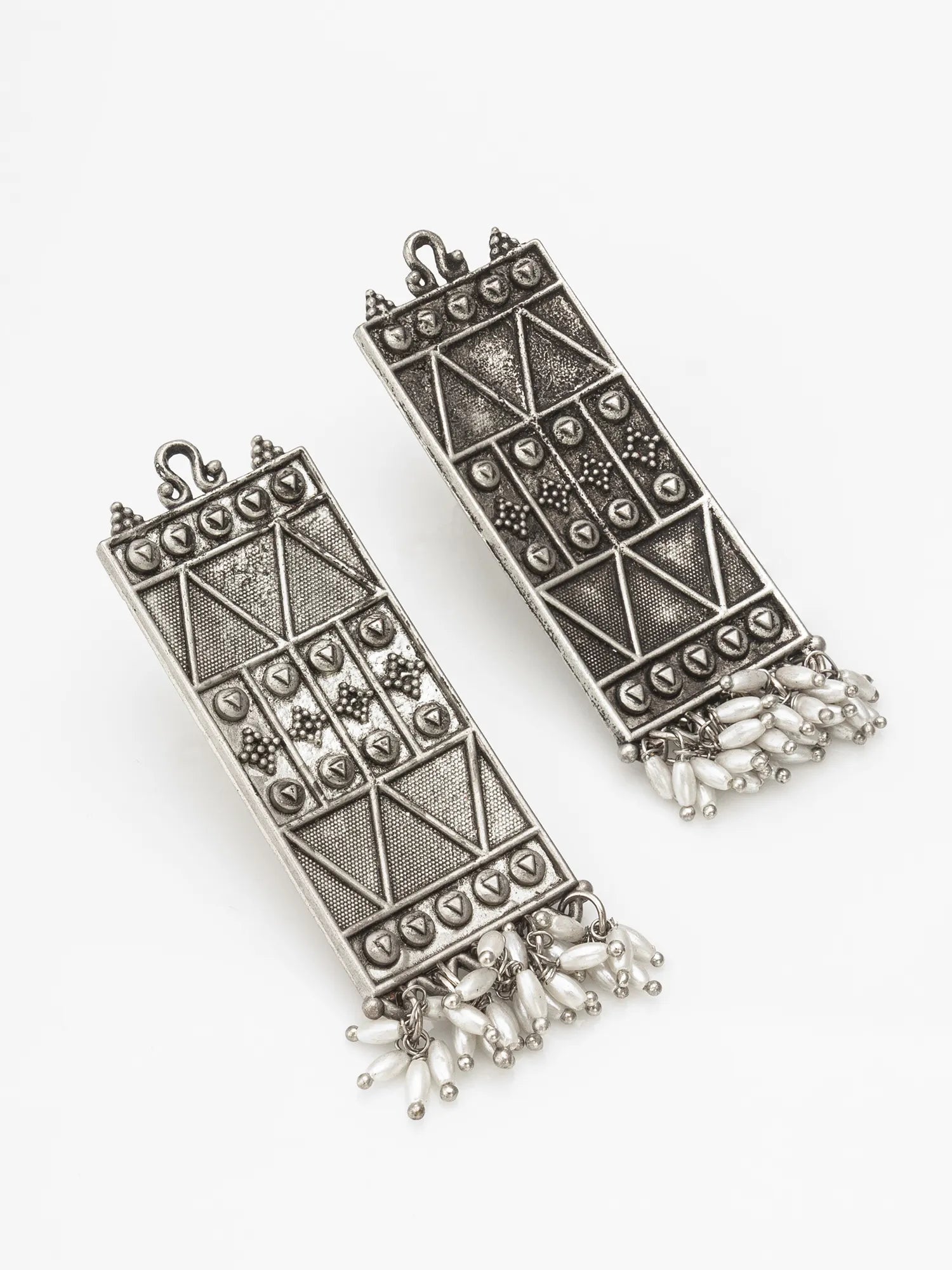 A pair of silver-toned rectangular pendant earrings with geometric engraved patterns and dangling bead fringe, shown on a plain white background.