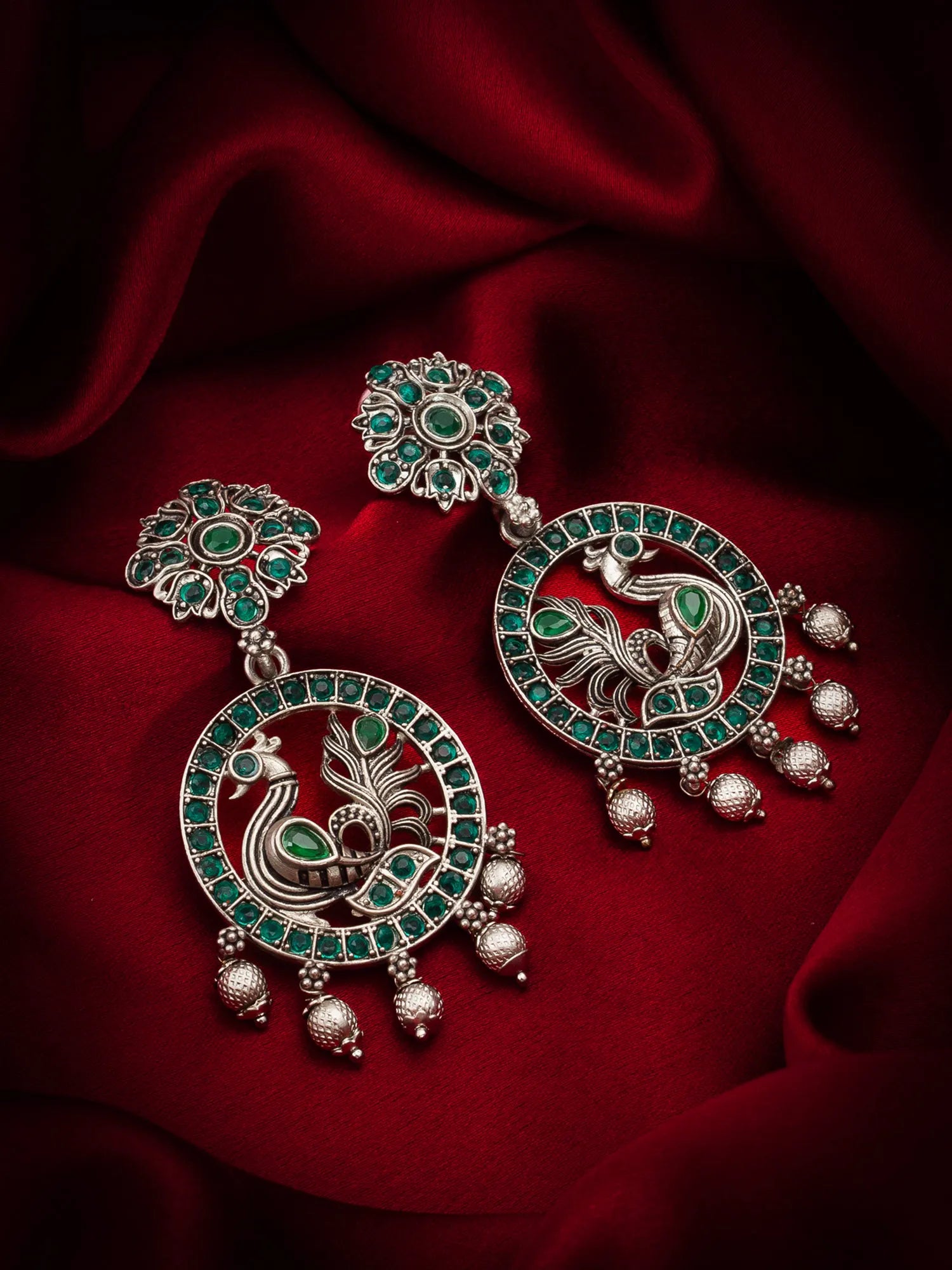Oxidized Peacock Chandbali Earrings On A Red Background