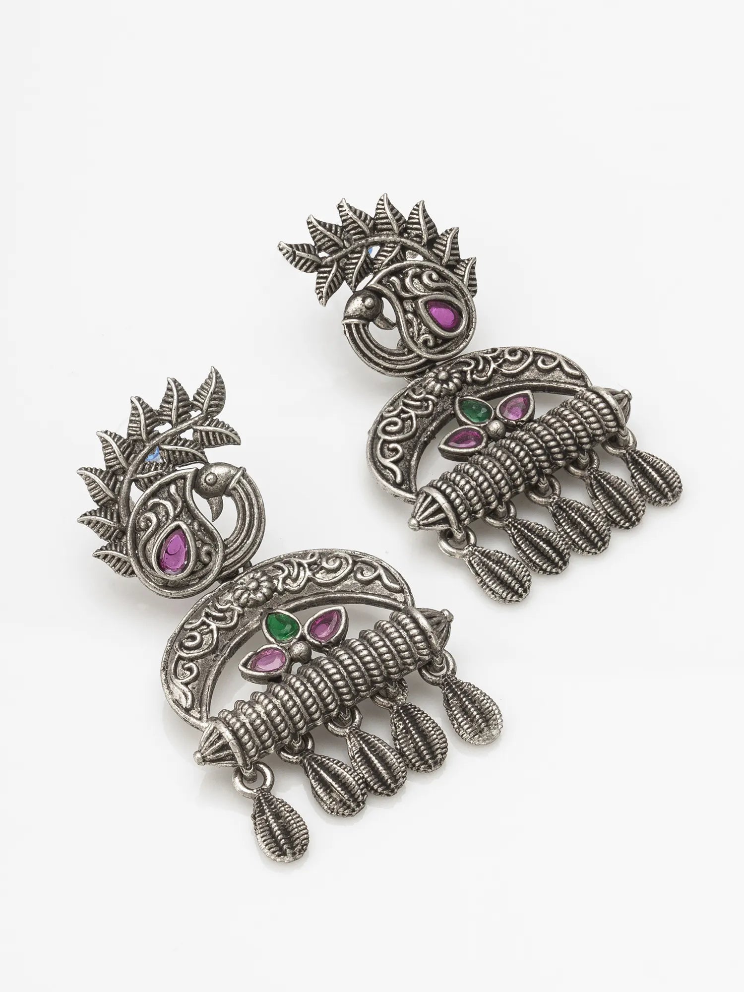 A pair of ornate silver-toned jhumka earrings with intricate filigree work and small pink and green stone accents, displayed on a clean white background.