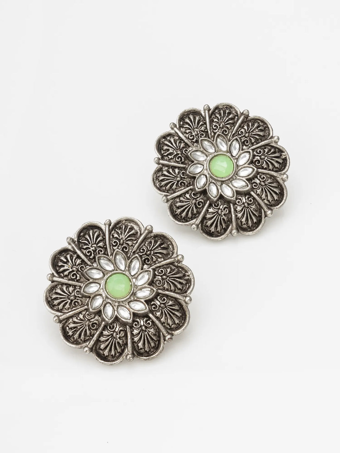 A pair of silver-toned filigree flower-shaped earrings with oval green centers, displayed on a draped deep red fabric background.