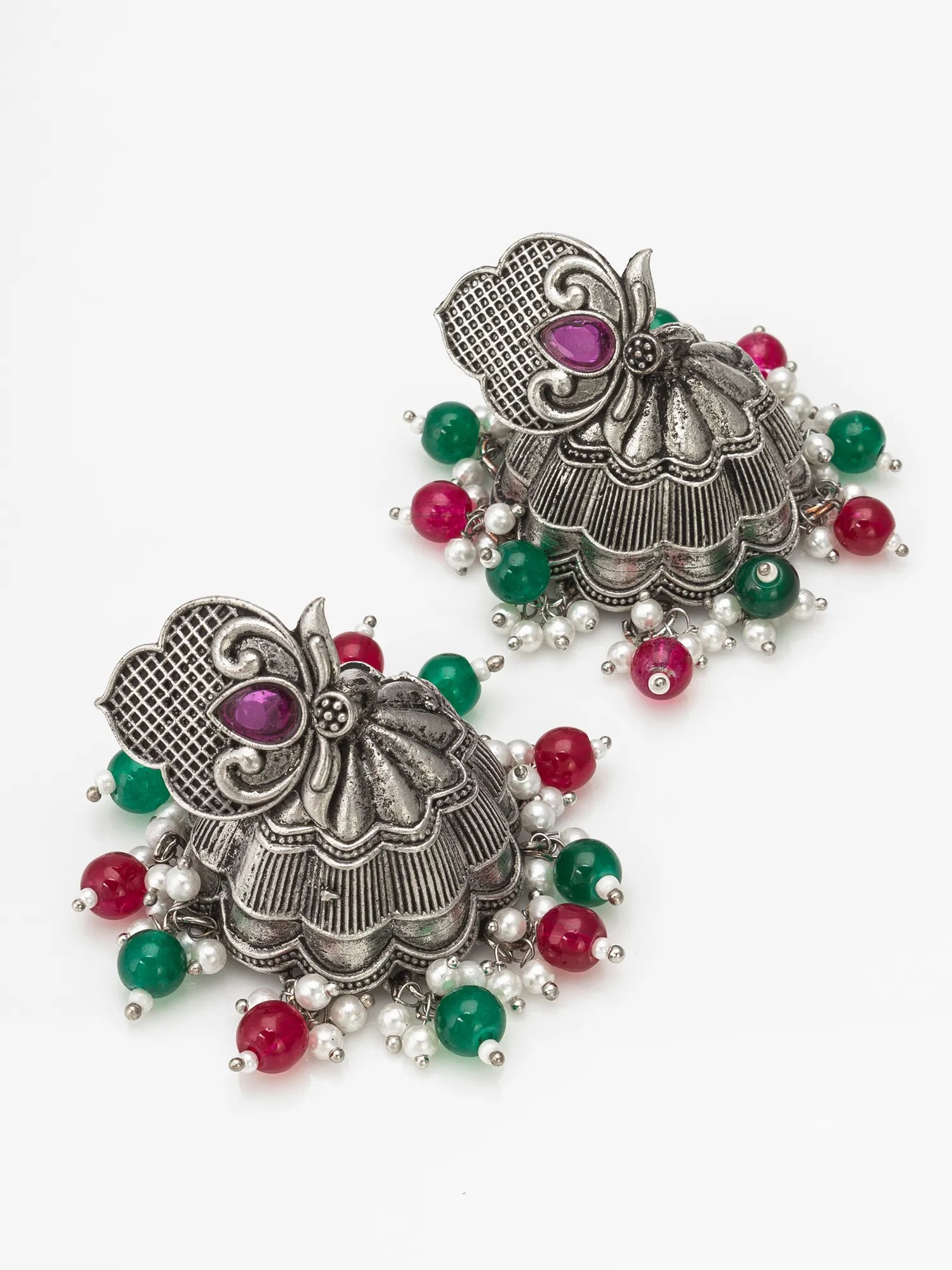 A pair of ornate silver-toned jhumka earrings decorated with red and green beads and pink gemstones, displayed on a clean white background.