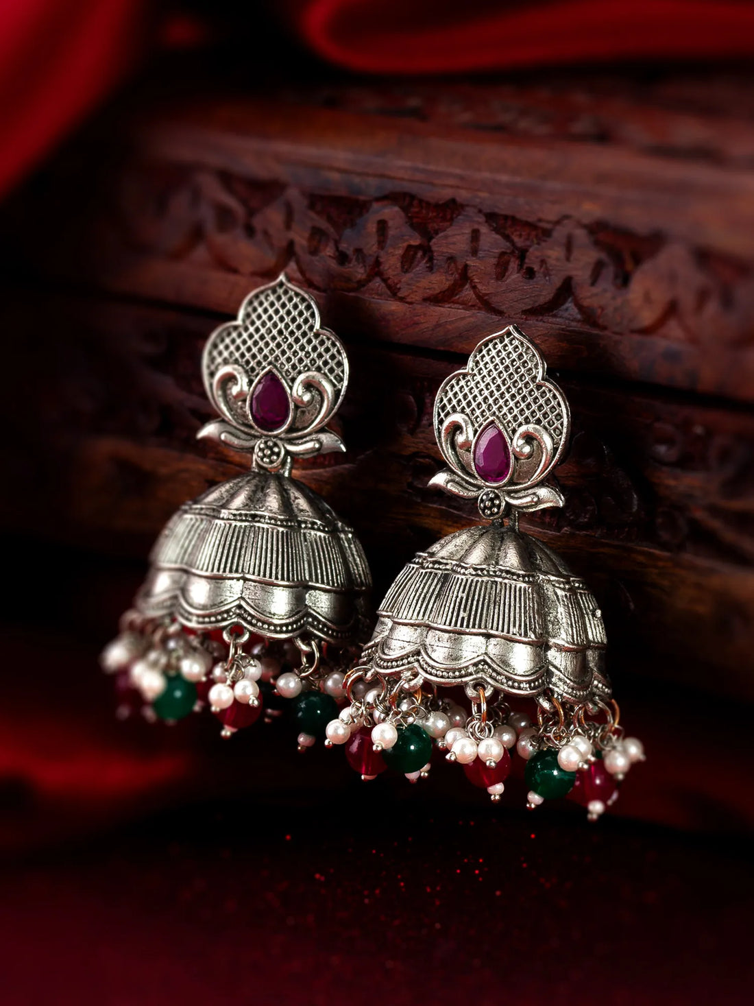 Silver jhumka earrings with red and green beads on a dark background