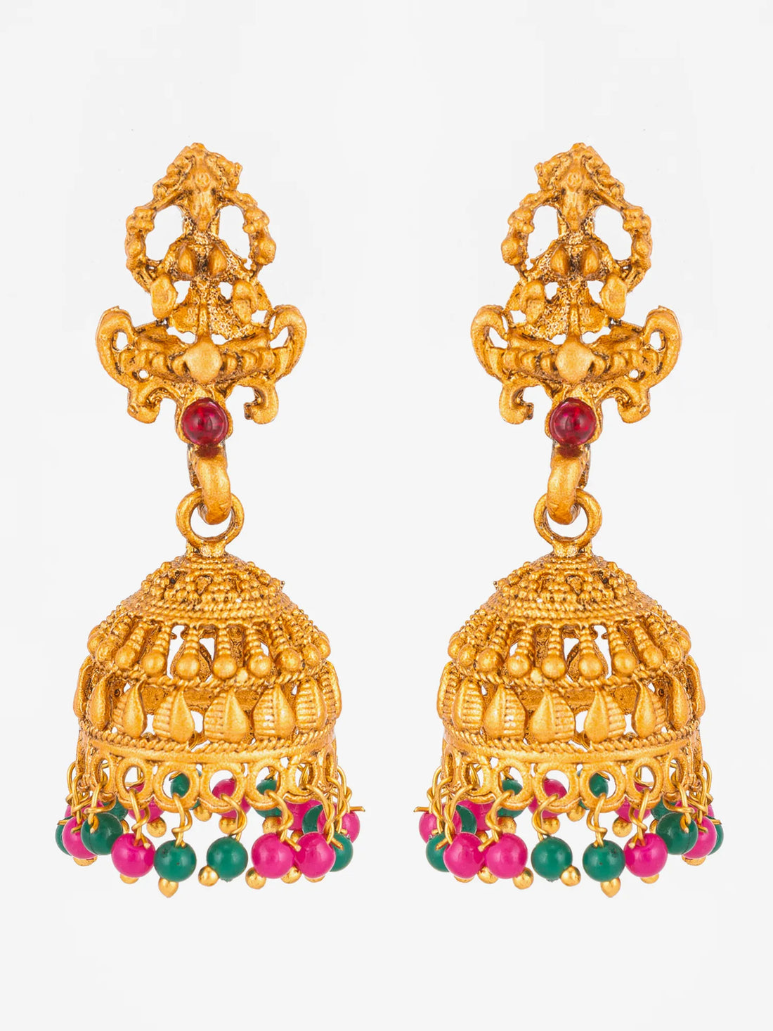 A pair of ornate gold-toned jhumka earrings with small red and green stone accents and dangling pink bead drops, displayed on a curved teal surface.