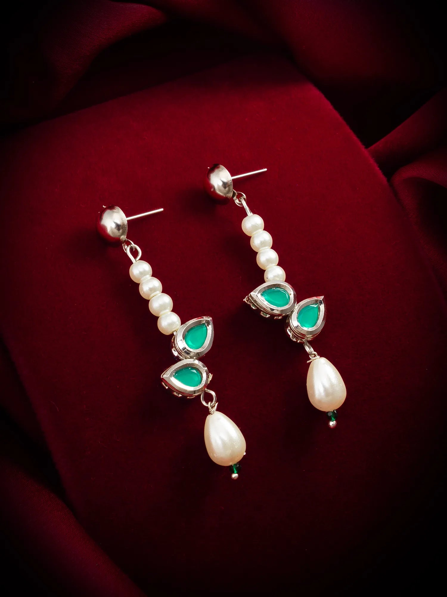 Pair of earrings with pearls and green gemstones on a red fabric background