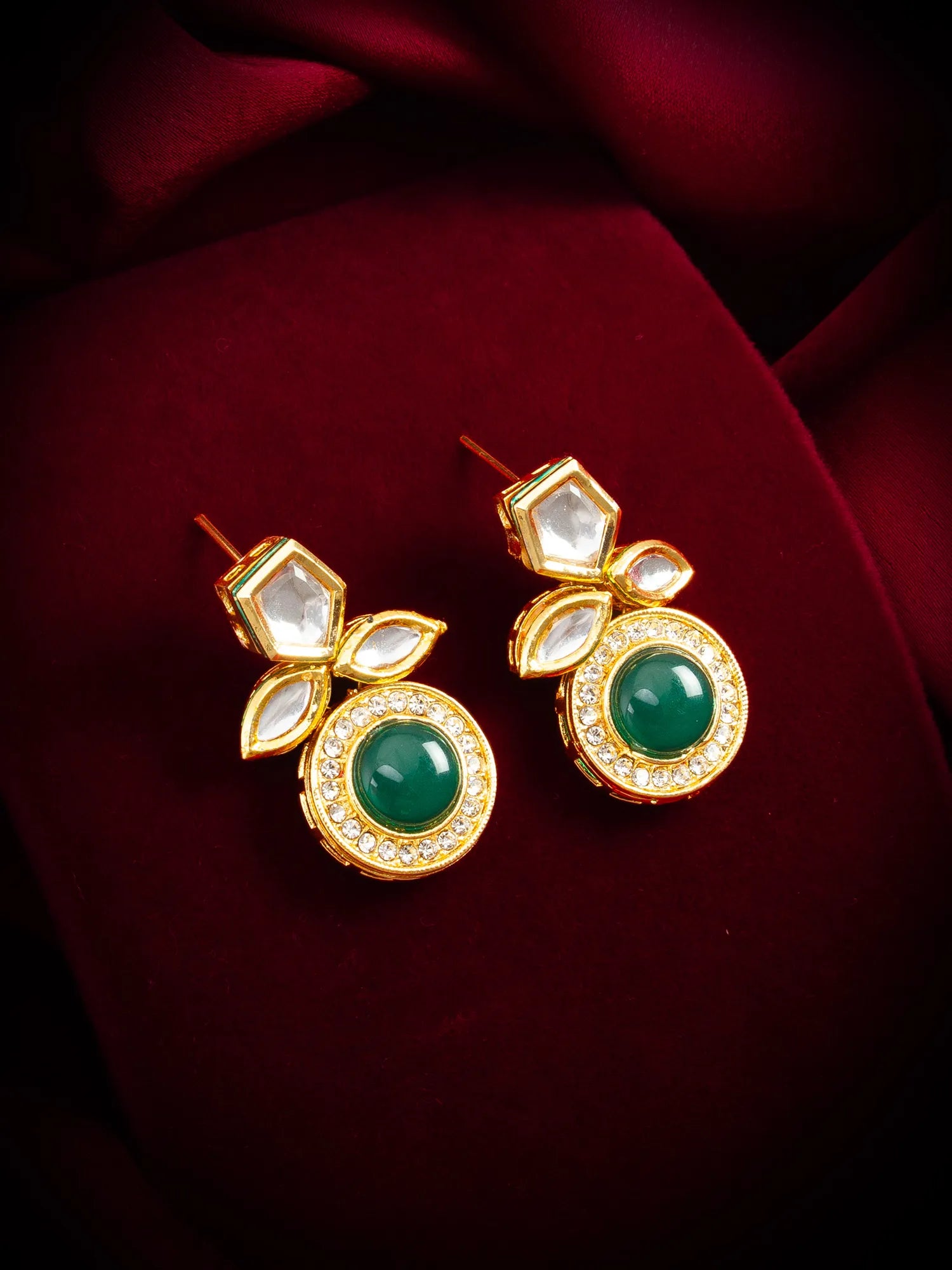 Gold earrings with green gemstones on a red fabric background