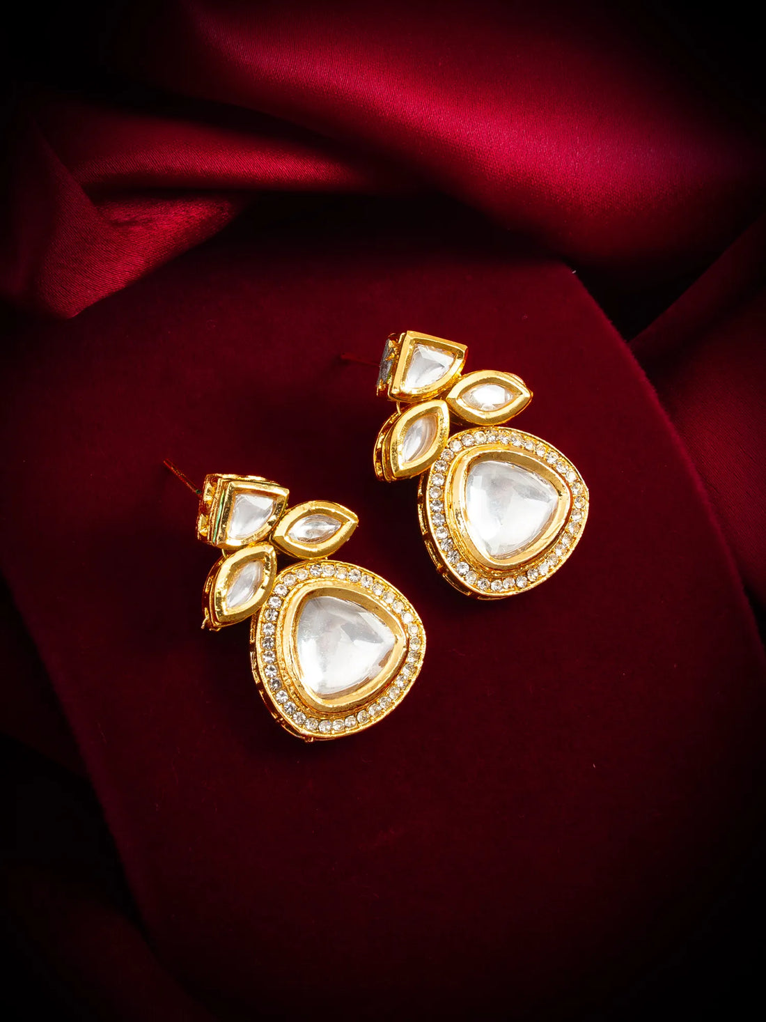 Gold earrings with heart-shaped gemstones on a red fabric background