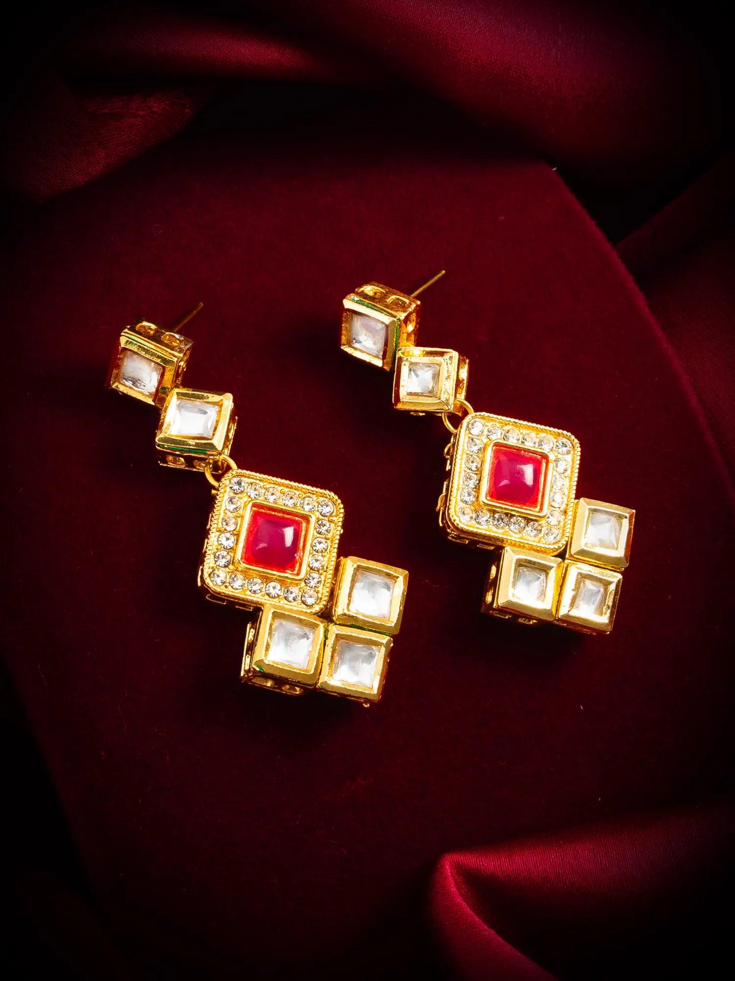 Gold earrings with red and clear gemstones on a red fabric background