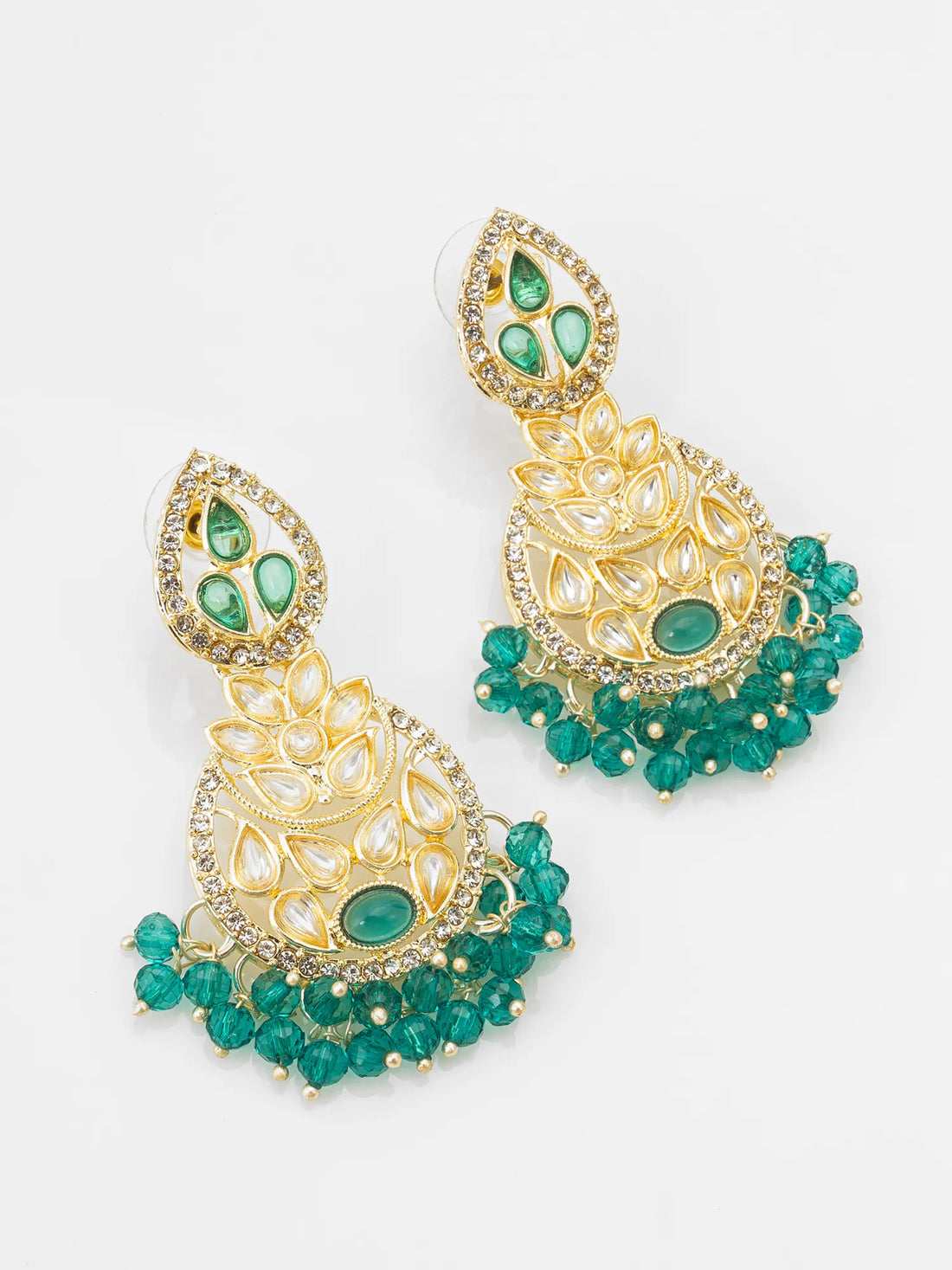 Ornate gold and green earrings on a teal background
