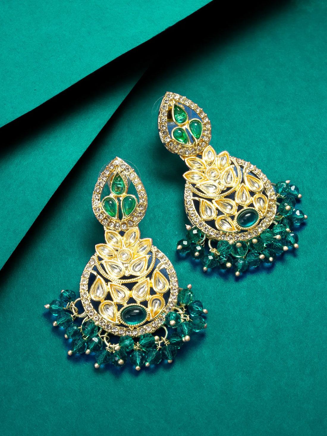 Ornate gold and green earrings on a teal background