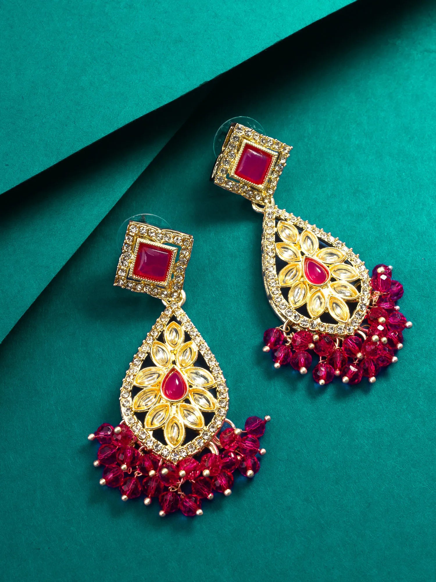 Ornate gold and red earrings on a teal background