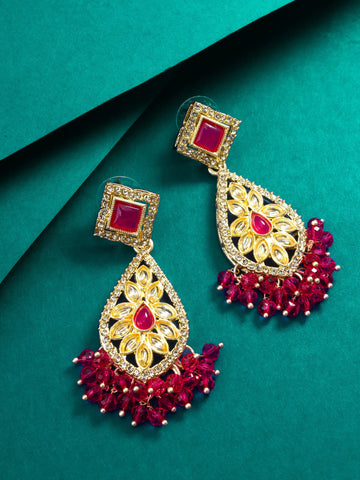 Ornate gold and red earrings on a teal background