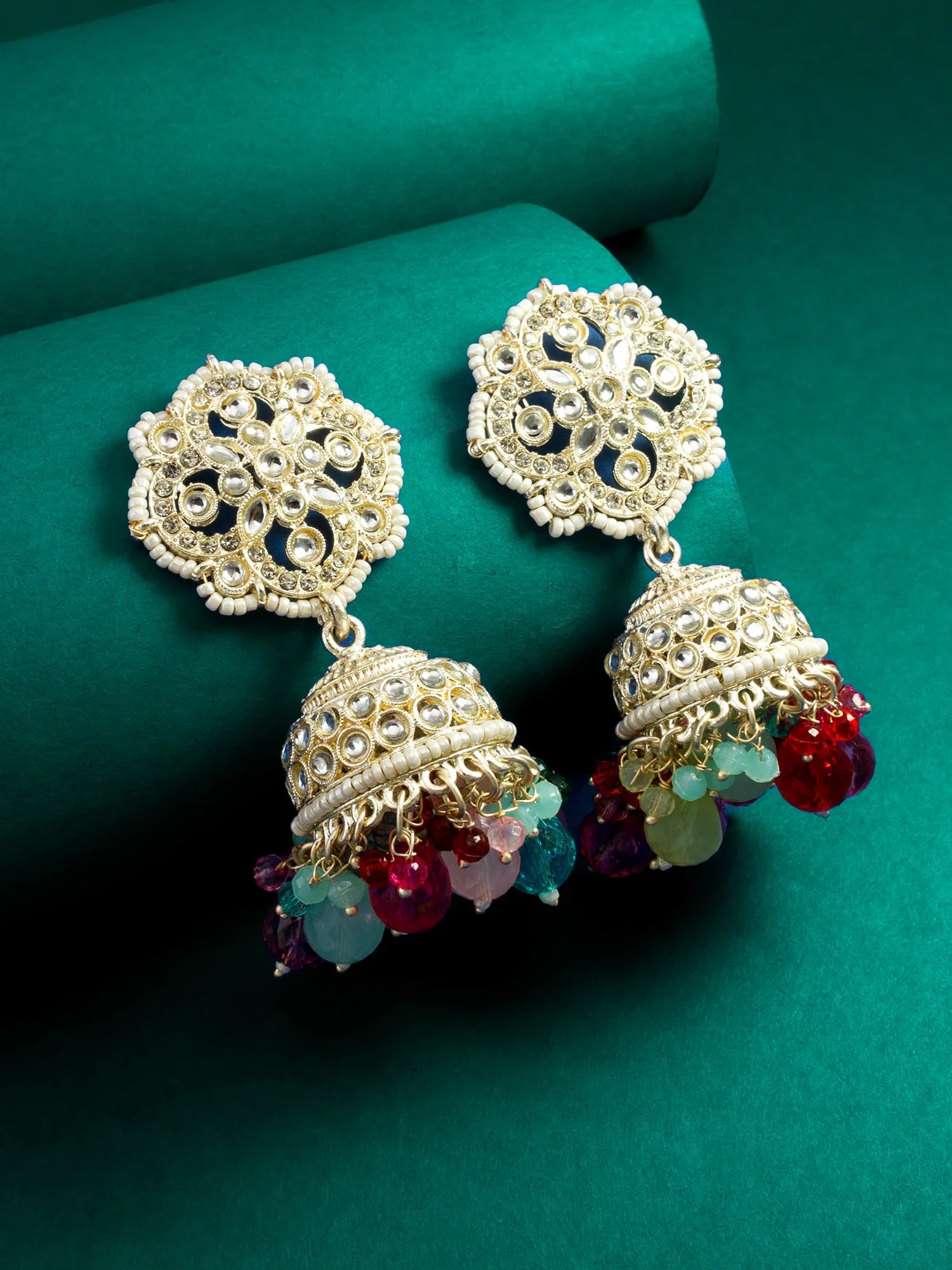 Ornate gold earrings with colorful beads on a green background