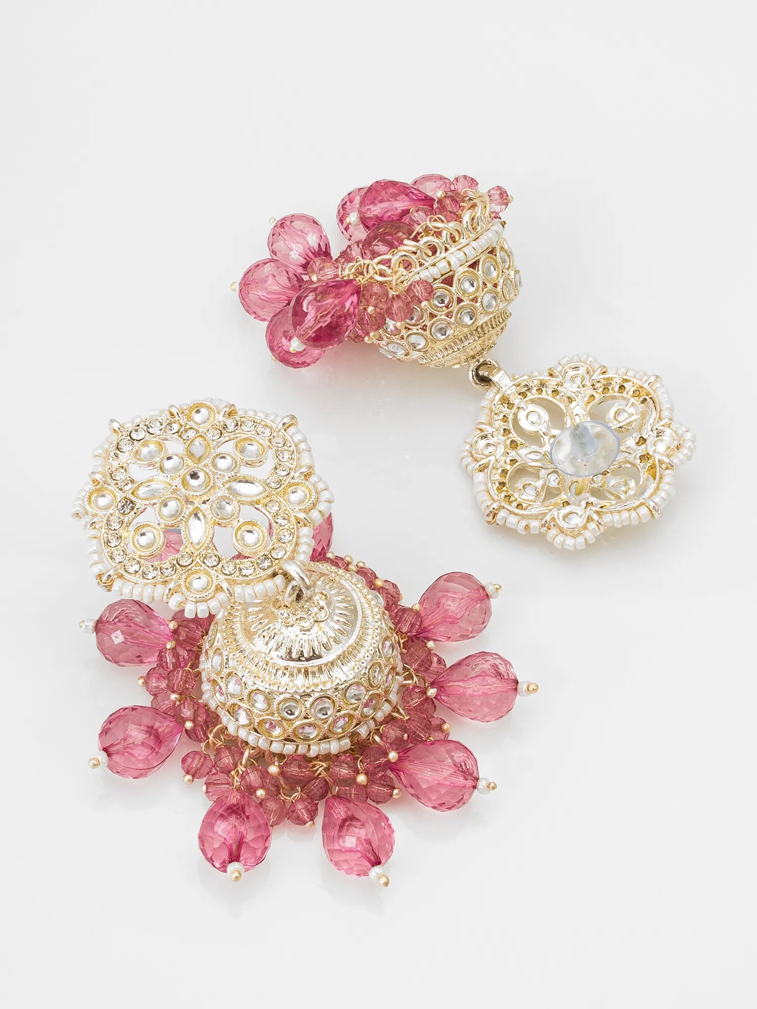 A pair of ornate gold-plated jhumka earrings decorated with pink faceted beads, small white pearls, and clear rhinestones, displayed on a clean white background.