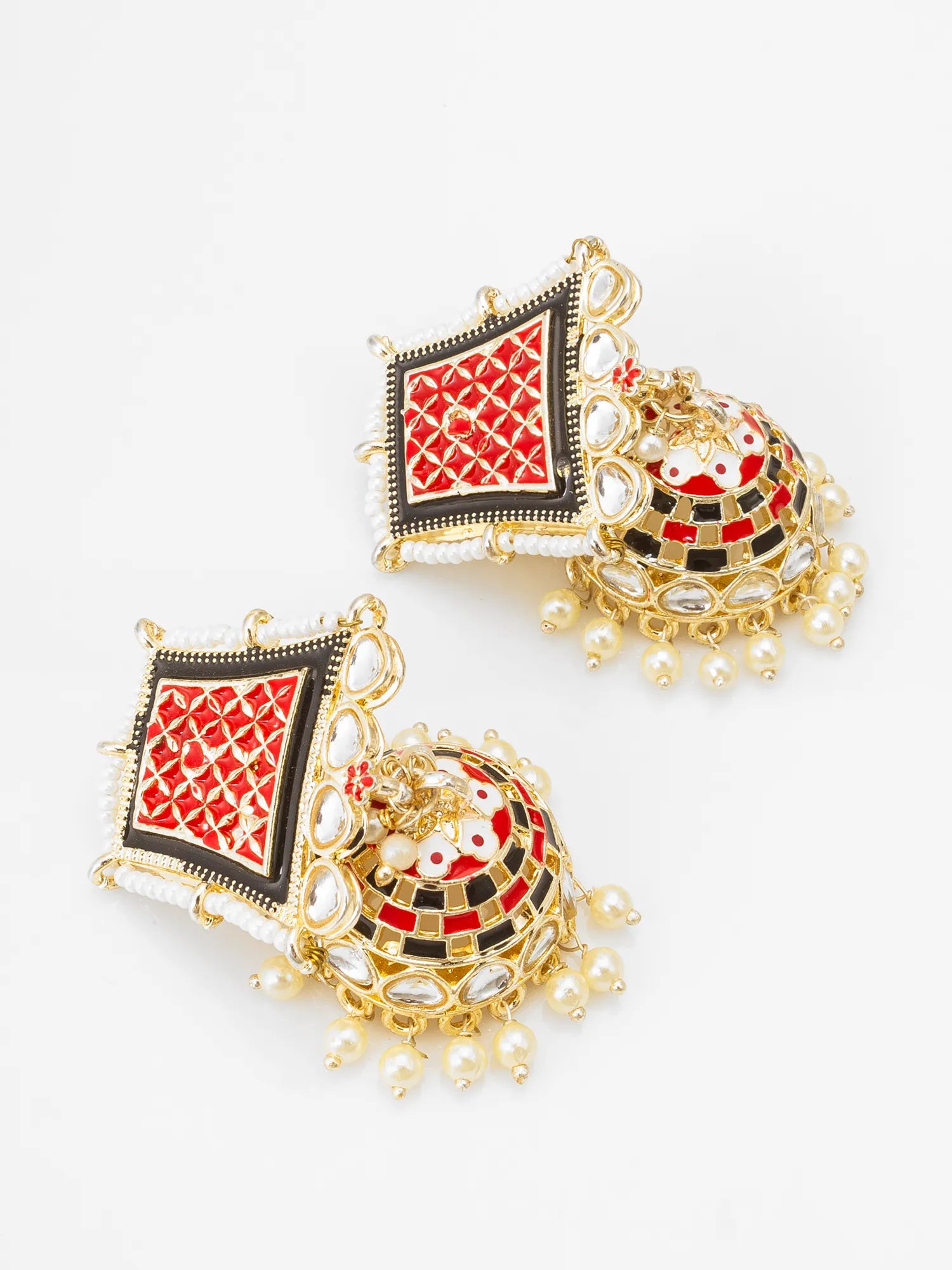 A pair of traditional Indian gold-plated jhumka earrings with red, black, and white enamel details and small pearl-like bead drops, shown on a plain white background.