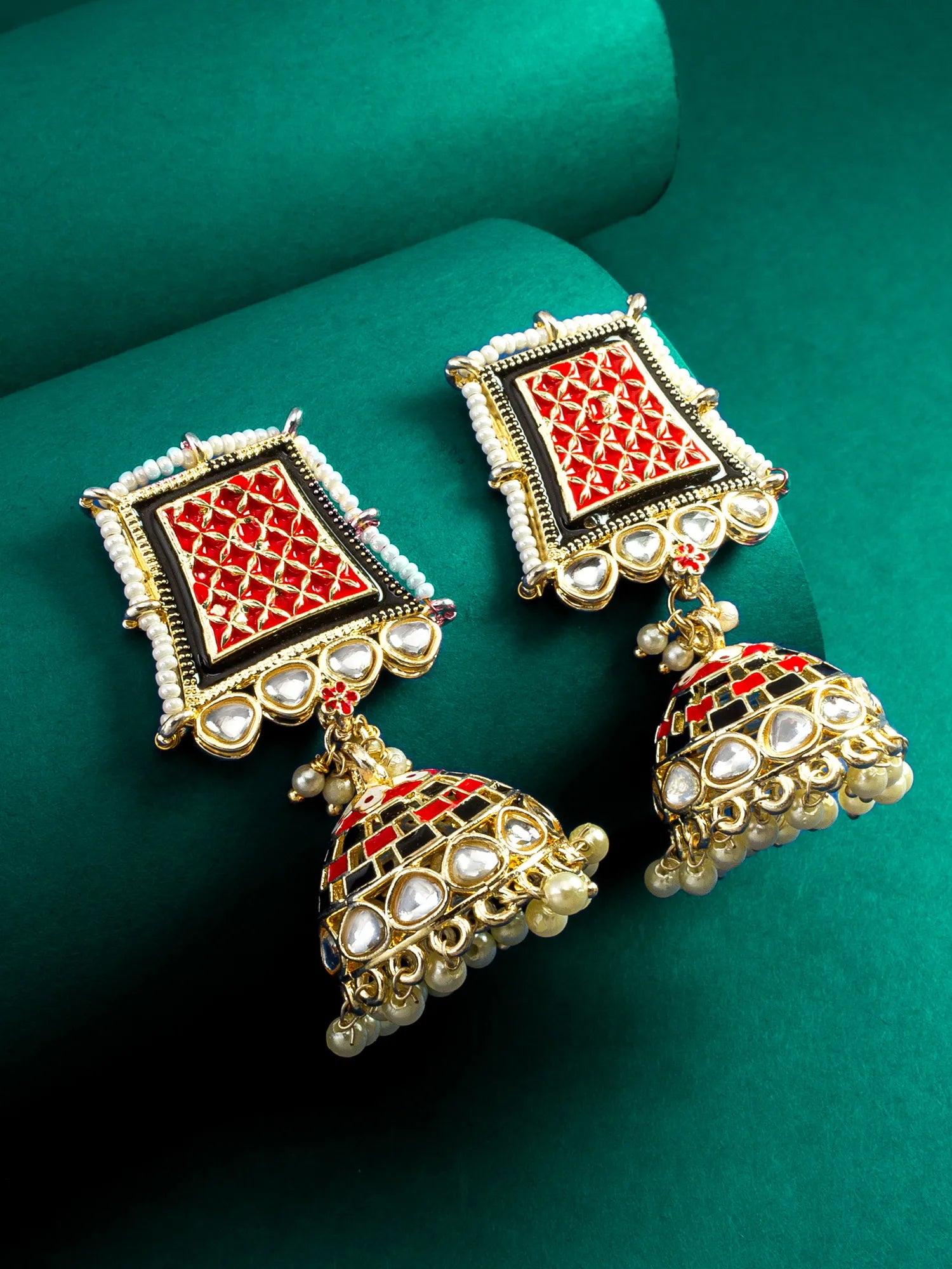 Ornate earrings with red and gold design on a green background