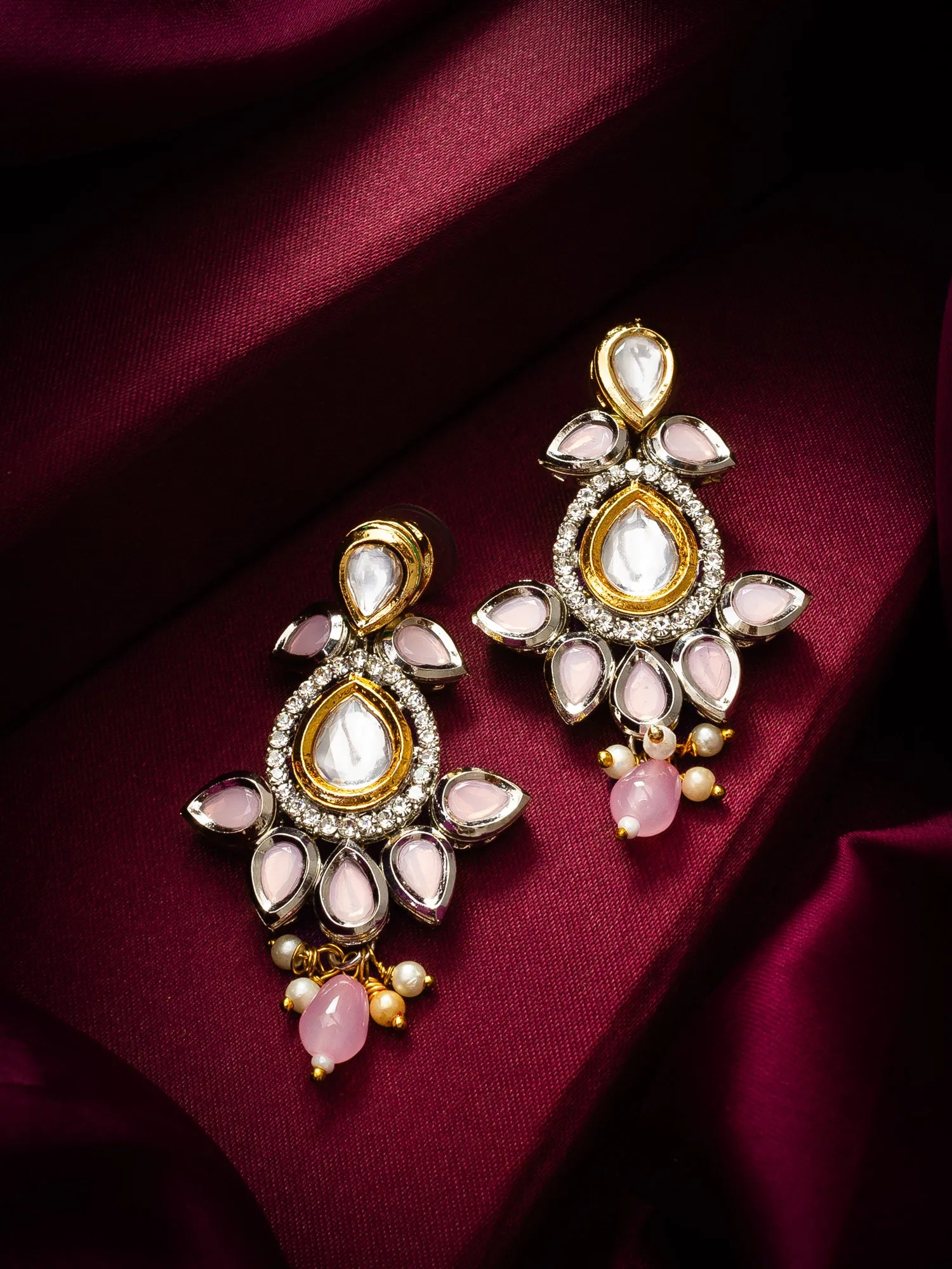 Ornate earrings with pink stones on a maroon fabric background