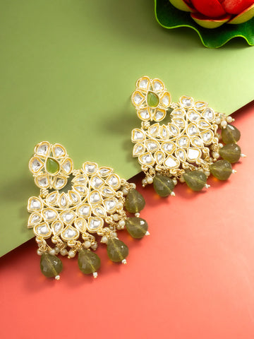 A pair of gold-toned traditional Indian jhumka earrings embellished with clear stone clusters and hanging olive green bead drops, displayed on a split green and coral background.