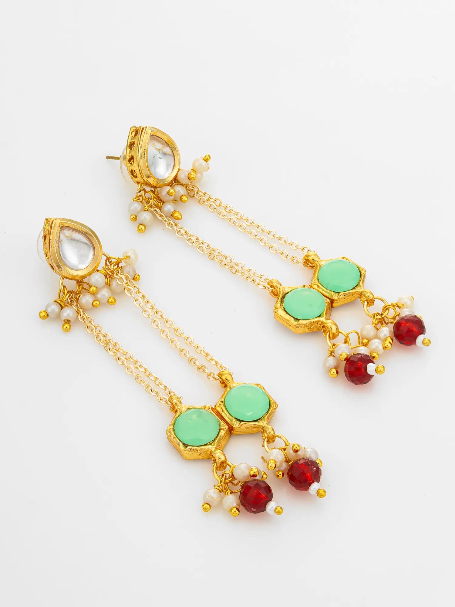 A pair of gold-plated dangle earrings featuring light green hexagonal stones, small white pearl-like beads, and dangling red faceted beads, displayed on a clean white background.