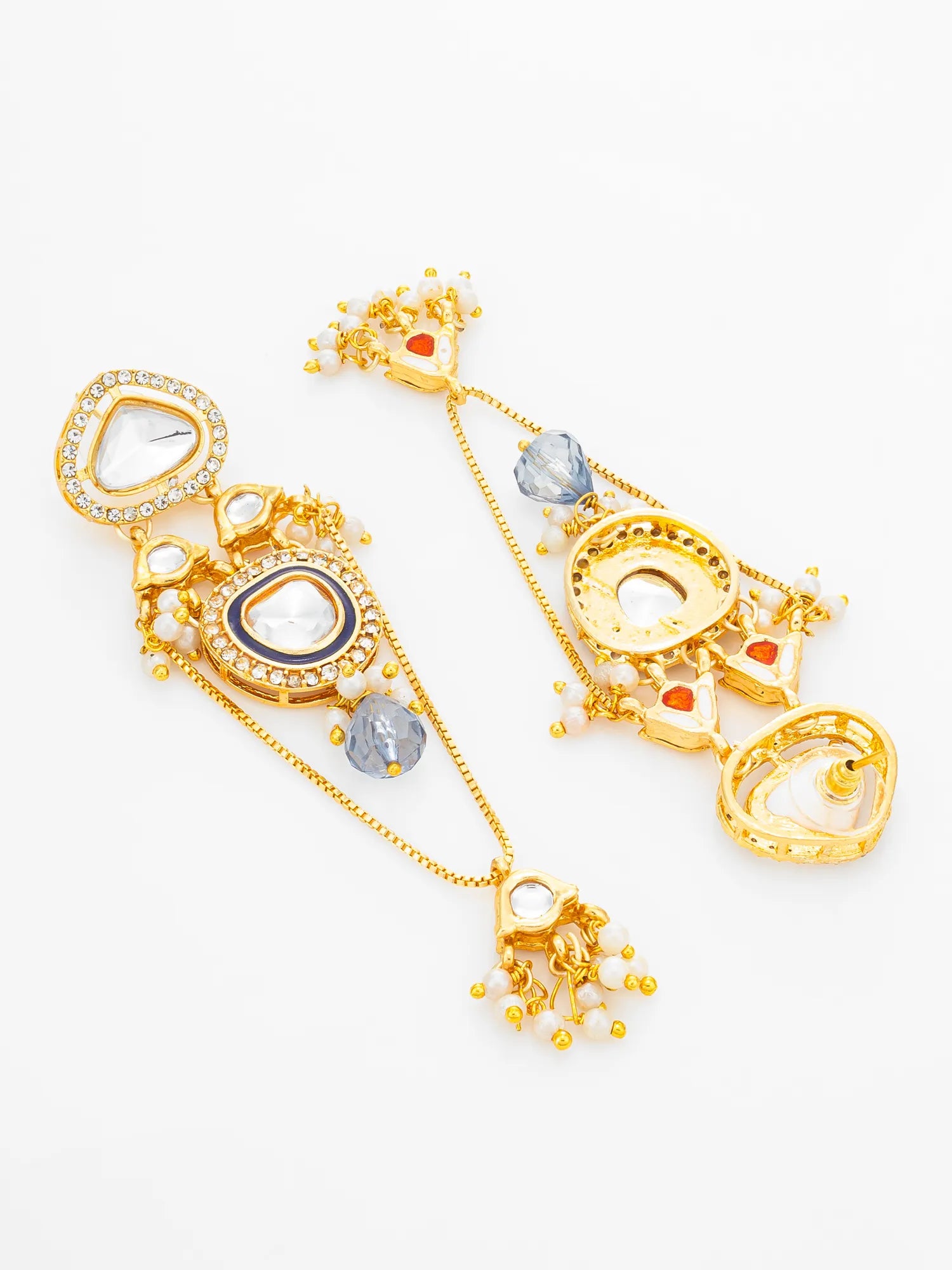 A pair of ornate gold-toned huggie earrings with intricate filigree, clear crystal details, white faux pearls, and small red and blue gemstone accents, displayed on a clean white background.