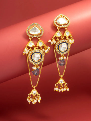 A pair of ornate gold-plated dangle earrings with white stones, small pearl-like bead accents, and purple teardrop charms, displayed against a red background.