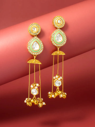 A pair of gold-plated Indian kanzum earrings with mint green enamel, white stones, and dangling gold chains with small gold bells, displayed on a red background.
