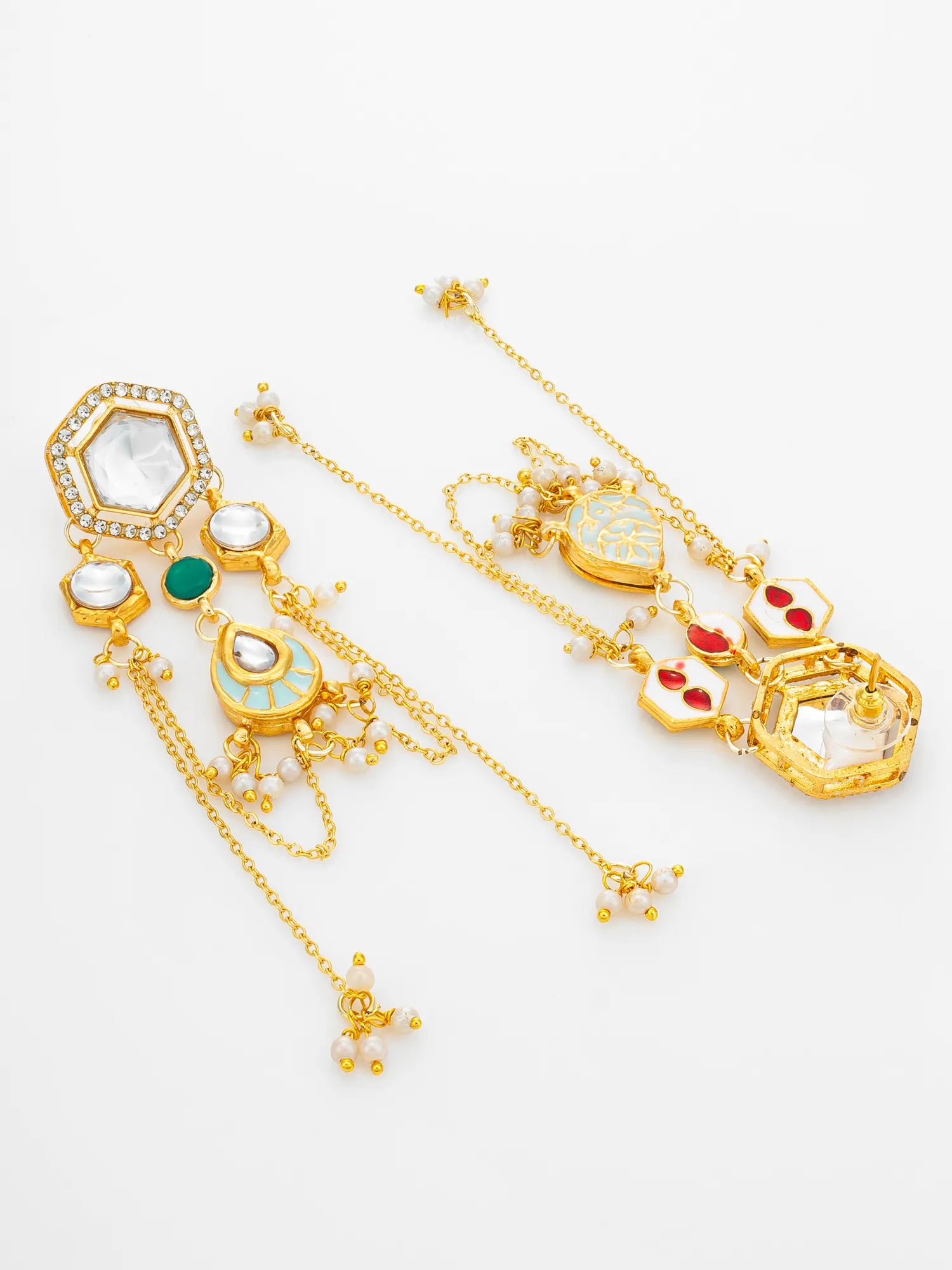 A pair of ornate gold-toned Indian style earrings with white stones, green and red enamel accents, and dangling chains on a white background.