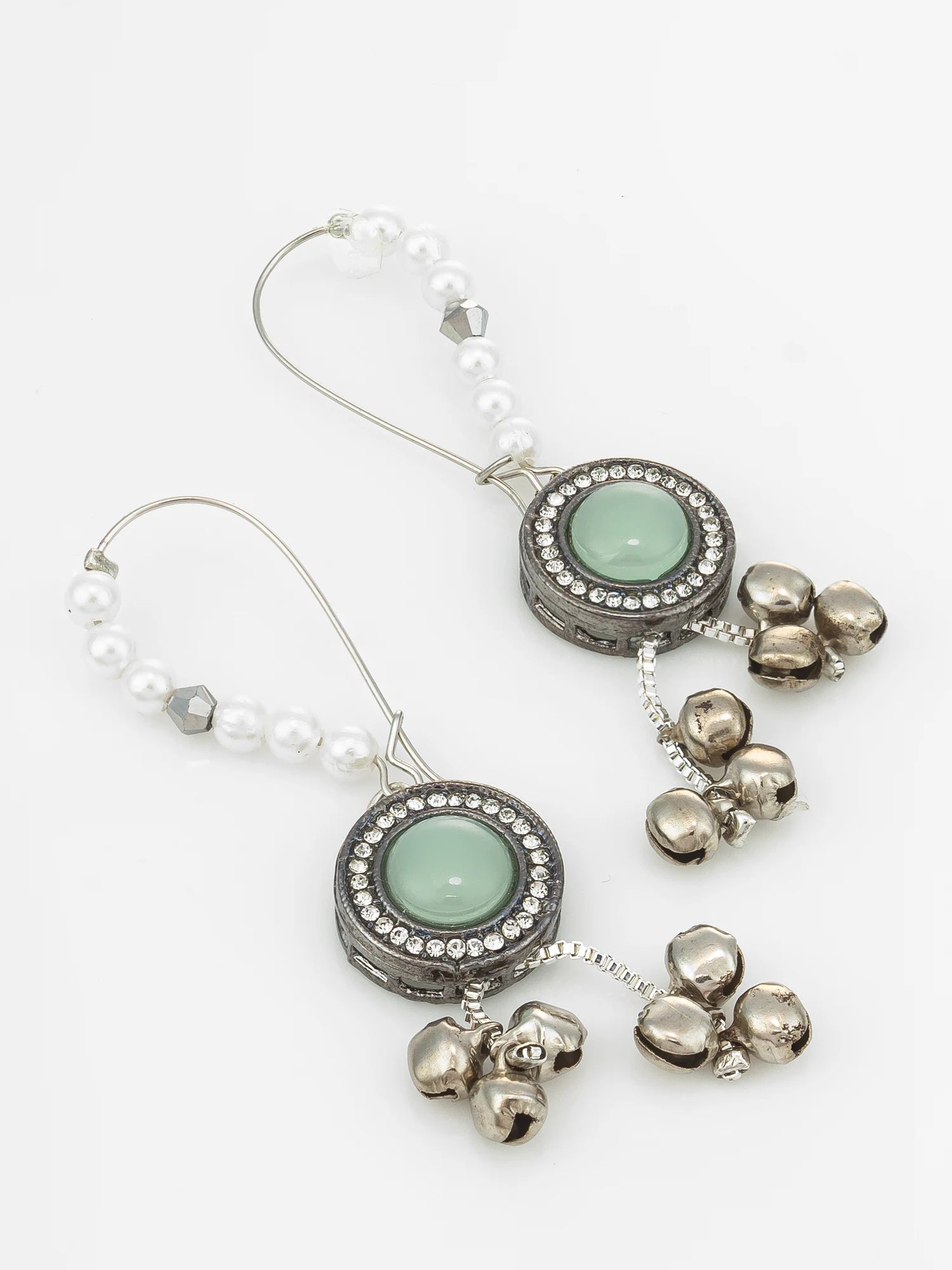 A pair of silver-toned dangle earrings with white pearl bead strands, oval green stone centers, rhinestone borders, and dangling silver bell charms, shown on a plain white background.