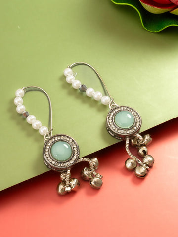 A pair of bohemian-style dangle earrings with white pearl beads, silver-toned metal, and round light green stone centers, shown on a split green and coral background.