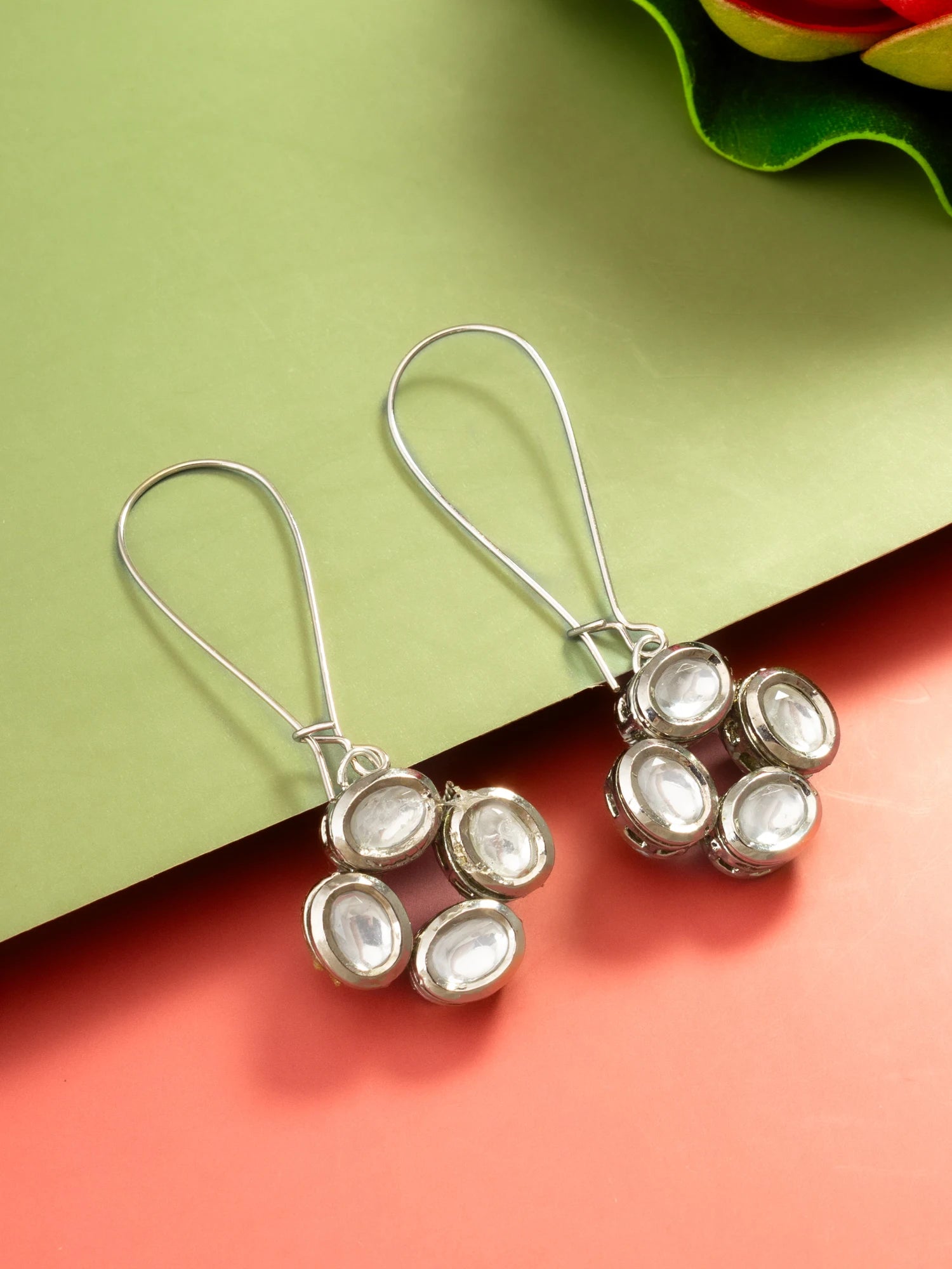 A pair of silver-toned dangle earrings with oval clear stones, displayed on a split green and coral background.