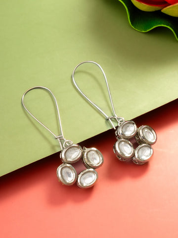 A pair of silver-toned dangle earrings with oval clear stones, displayed on a split green and coral background.