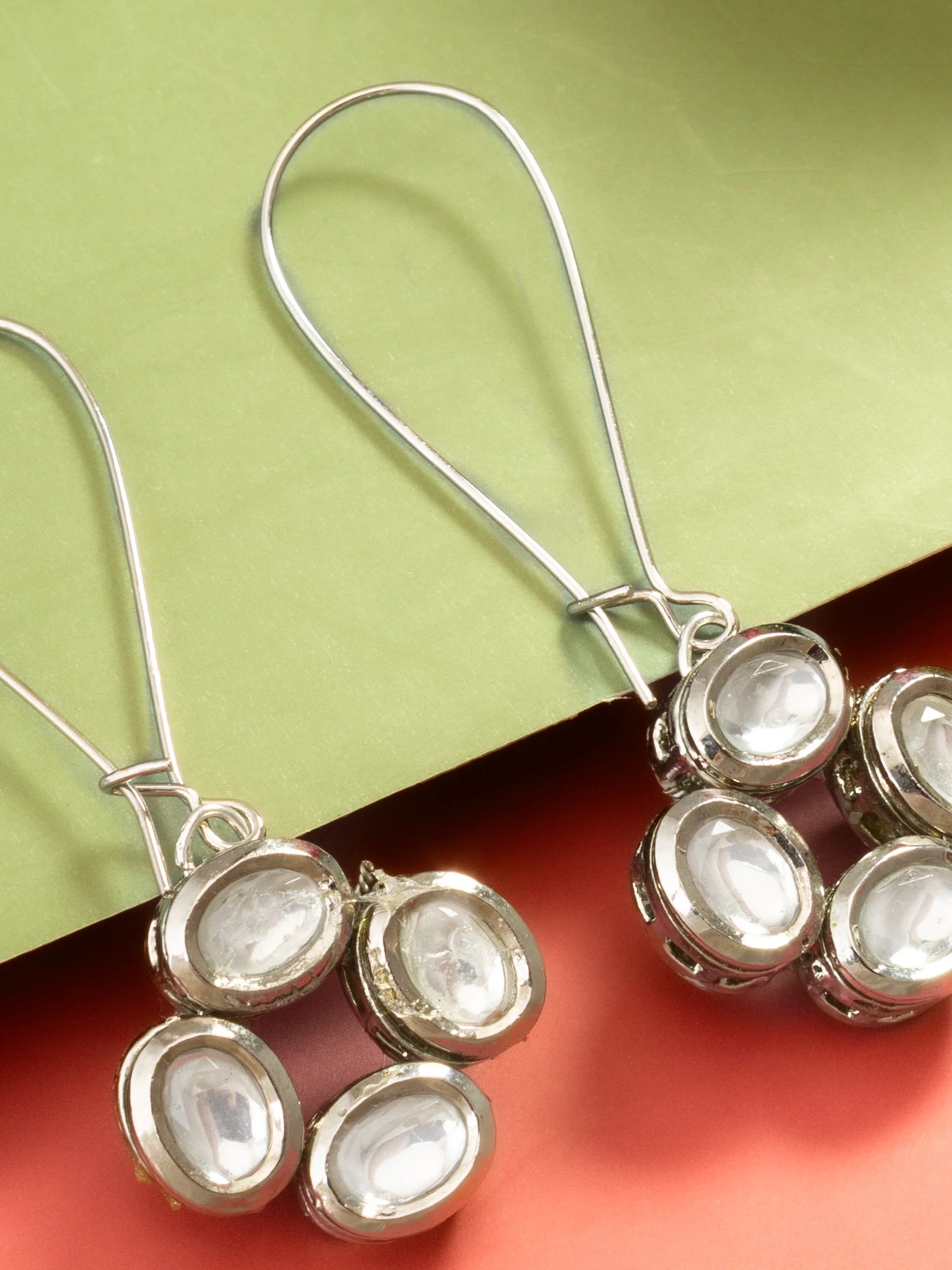 Silver dangle earrings with oval clear stone settings, shown close up against a split green and coral background.