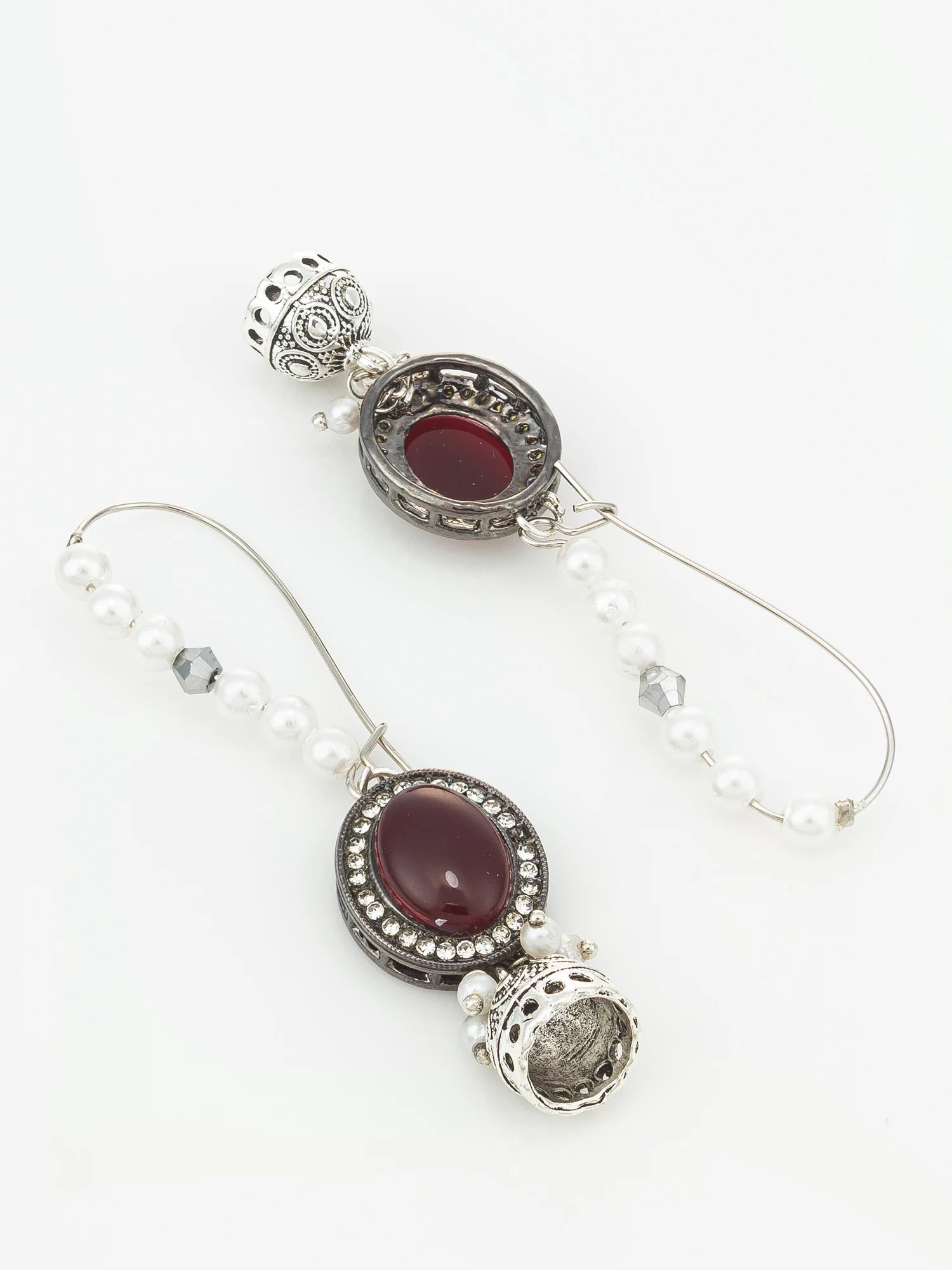 A pair of silver-toned dangle earrings featuring oval dark red gemstones, white pearl beads, and ornate filigree details, displayed on a clean white background.
