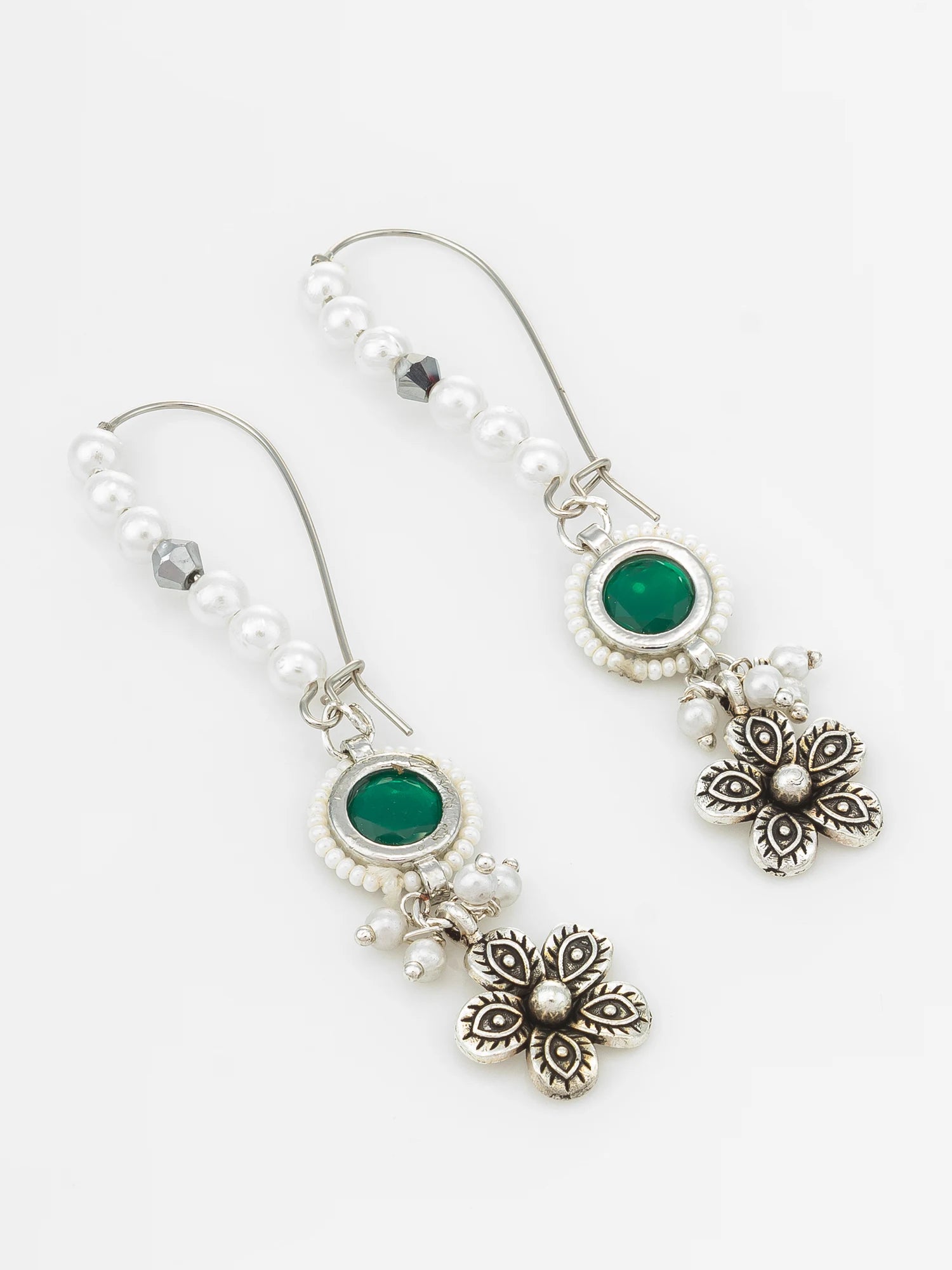A pair of silver-toned dangle earrings featuring white pearl beads, oval green gemstones, and ornate floral charms, displayed on a clean white background.