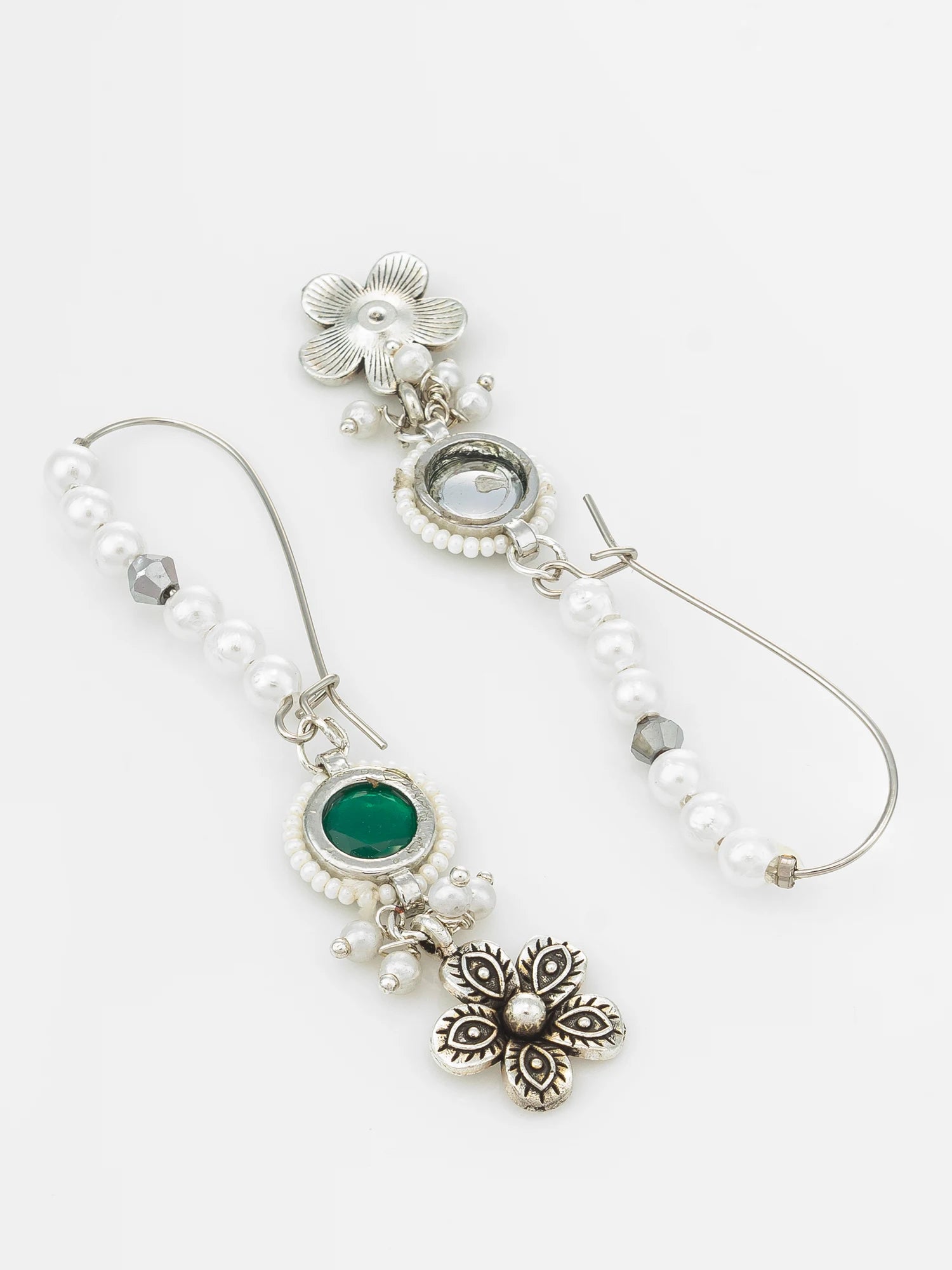 A pair of silver-toned dangle earrings with white pearl beads, a green oval stone, and a silver floral charm, displayed on a light gray background.
