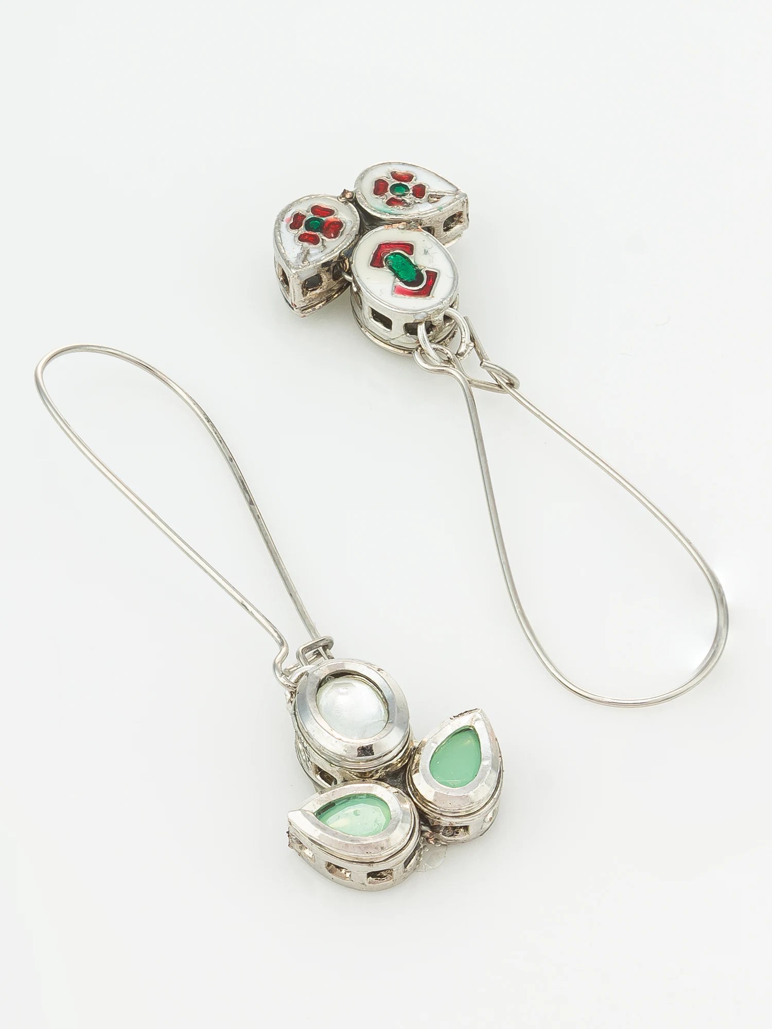 A pair of silver-toned dangle earrings with white enamel, red and green inlaid details, and teardrop-shaped green stone accents, displayed on a clean white background.